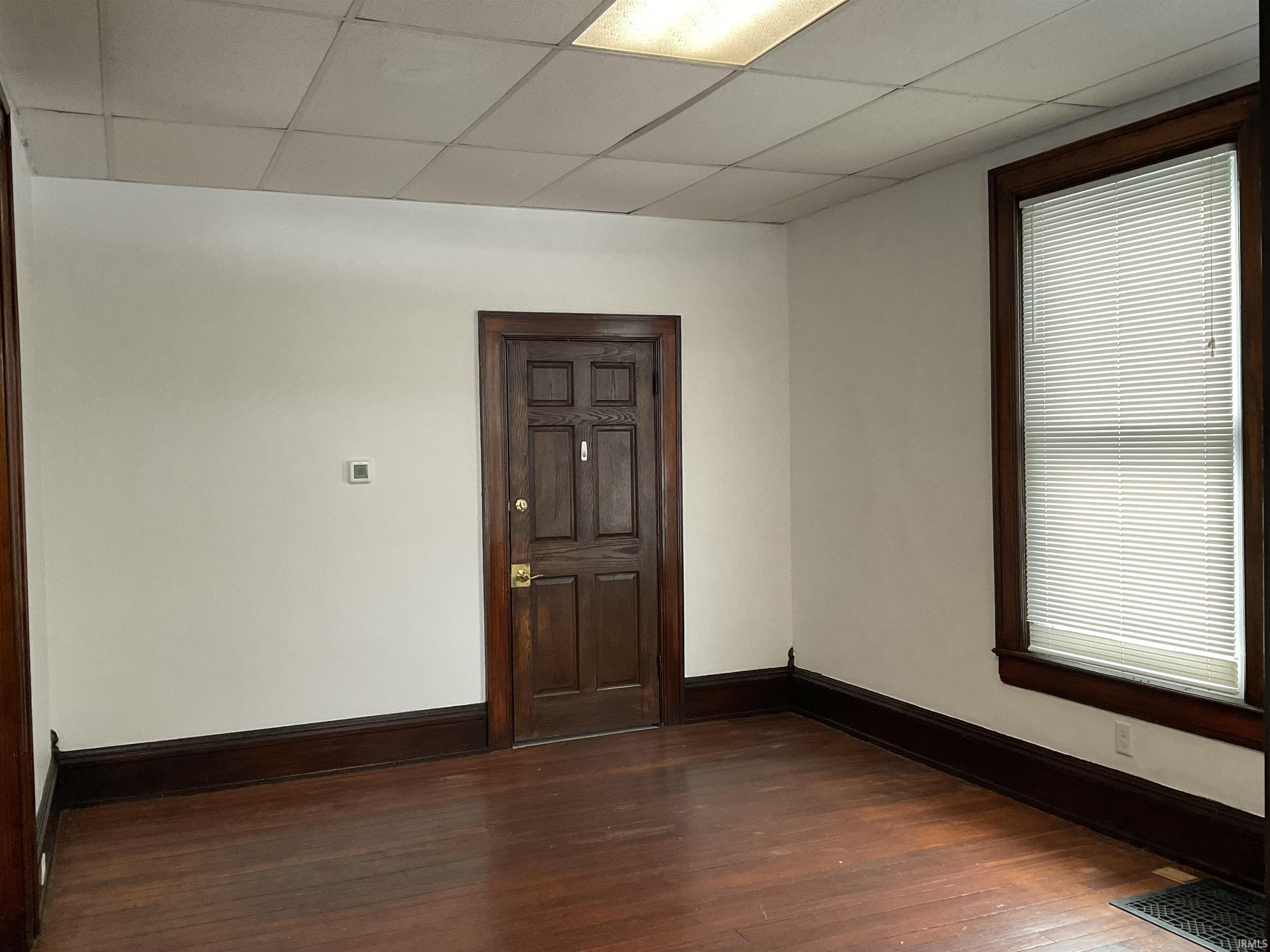 Unfurnished room with dark wood-style flooring and a drop ceiling