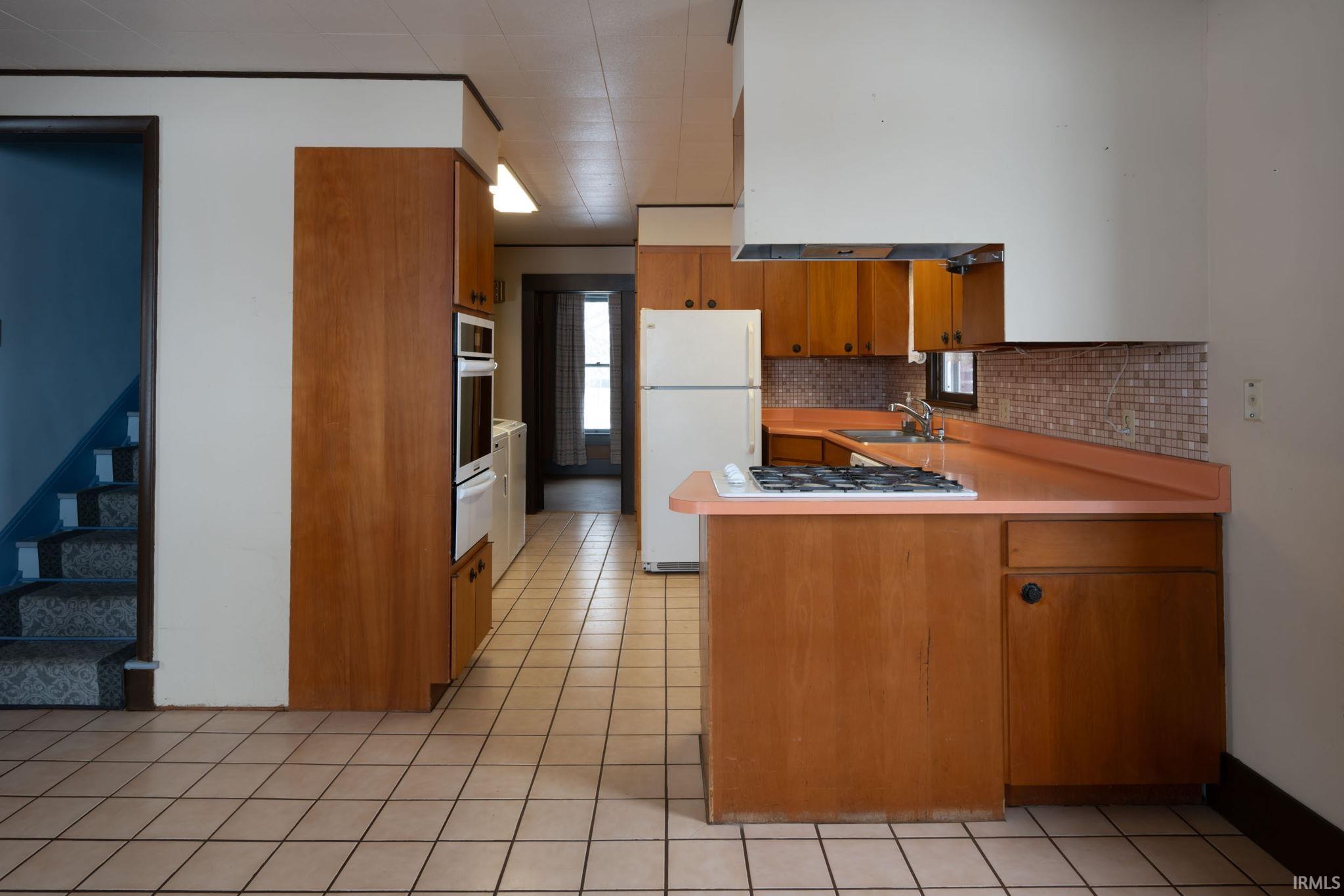 Kitchen with brown cabinetry, a peninsula, light countertops, backsplash, and freestanding refrigerator