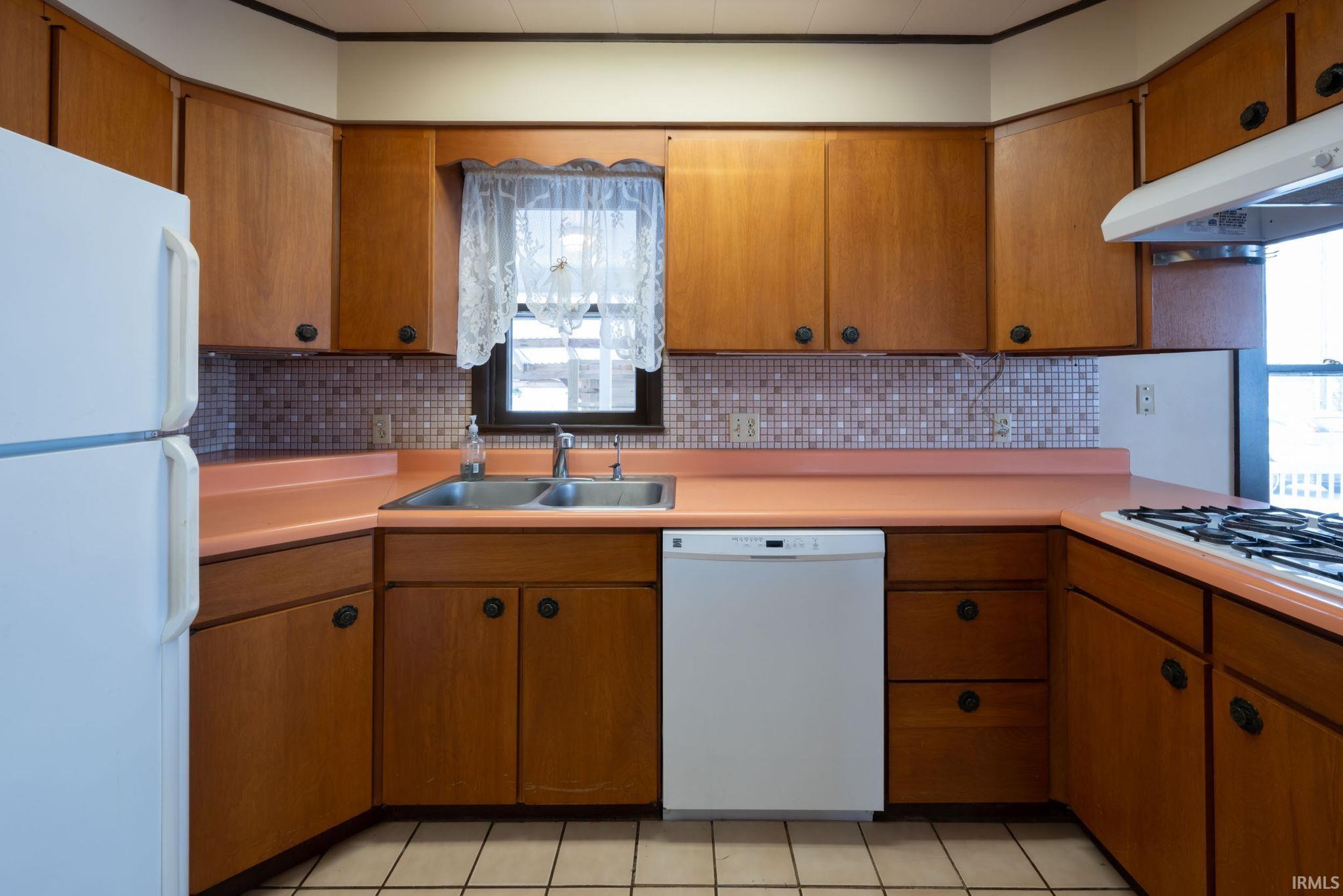 Kitchen with white appliances, decorative backsplash, and light countertops
