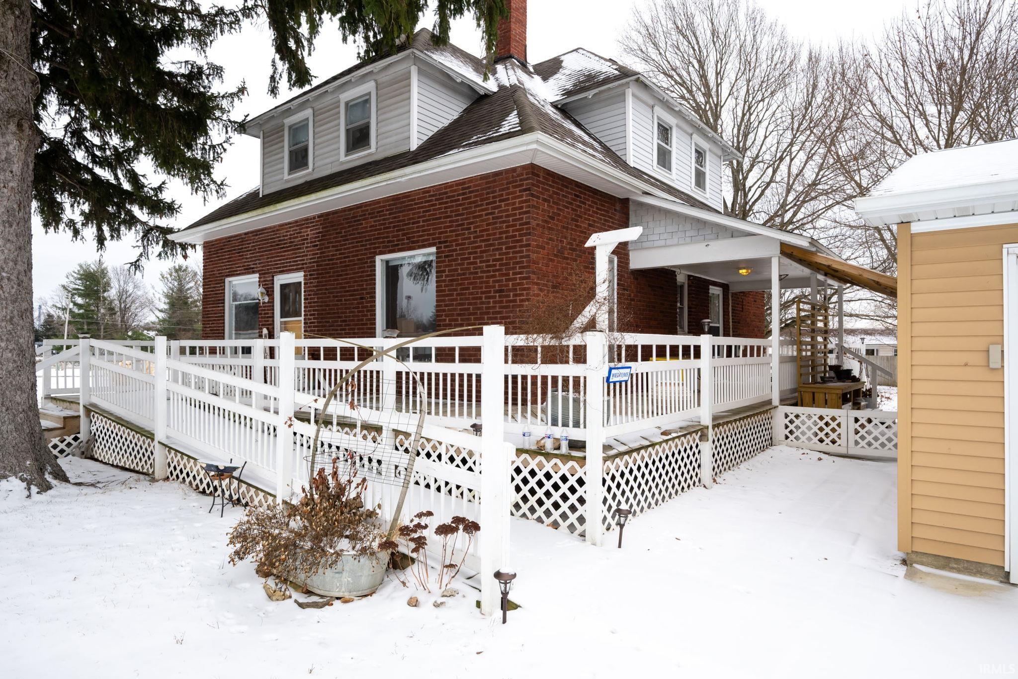 View of front facade with a wooden deck, brick siding, and a chimney