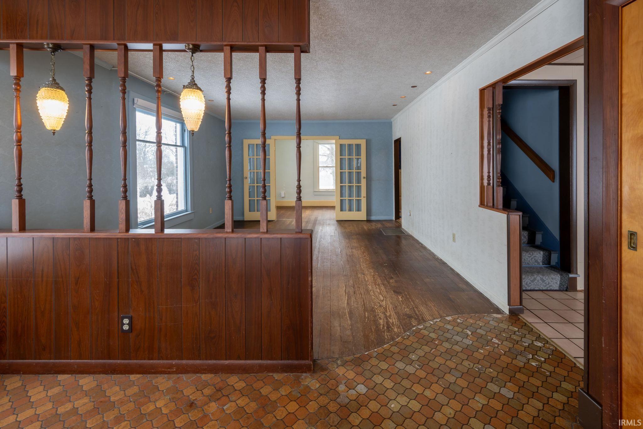 Unfurnished living room featuring tile patterned flooring, stairway, a textured ceiling, plenty of natural light, and crown molding