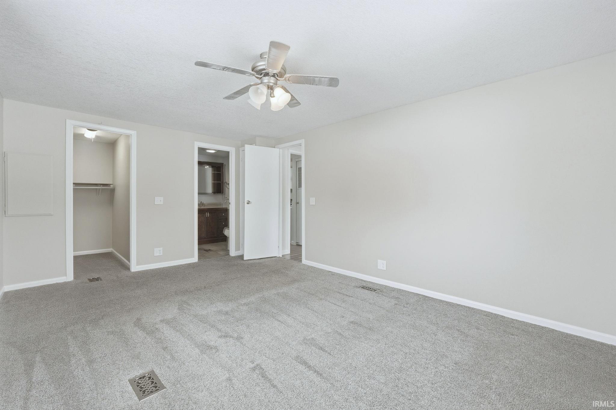 Unfurnished bedroom with a walk in closet, ensuite bathroom, carpet flooring, a ceiling fan, and a textured ceiling