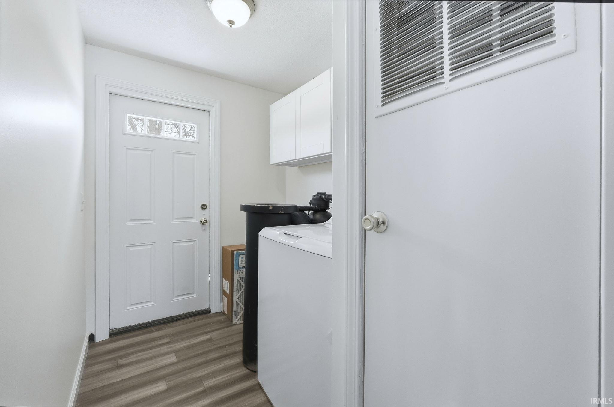 Washroom featuring dark wood-type flooring, washer / clothes dryer, cabinet space, and a heating unit
