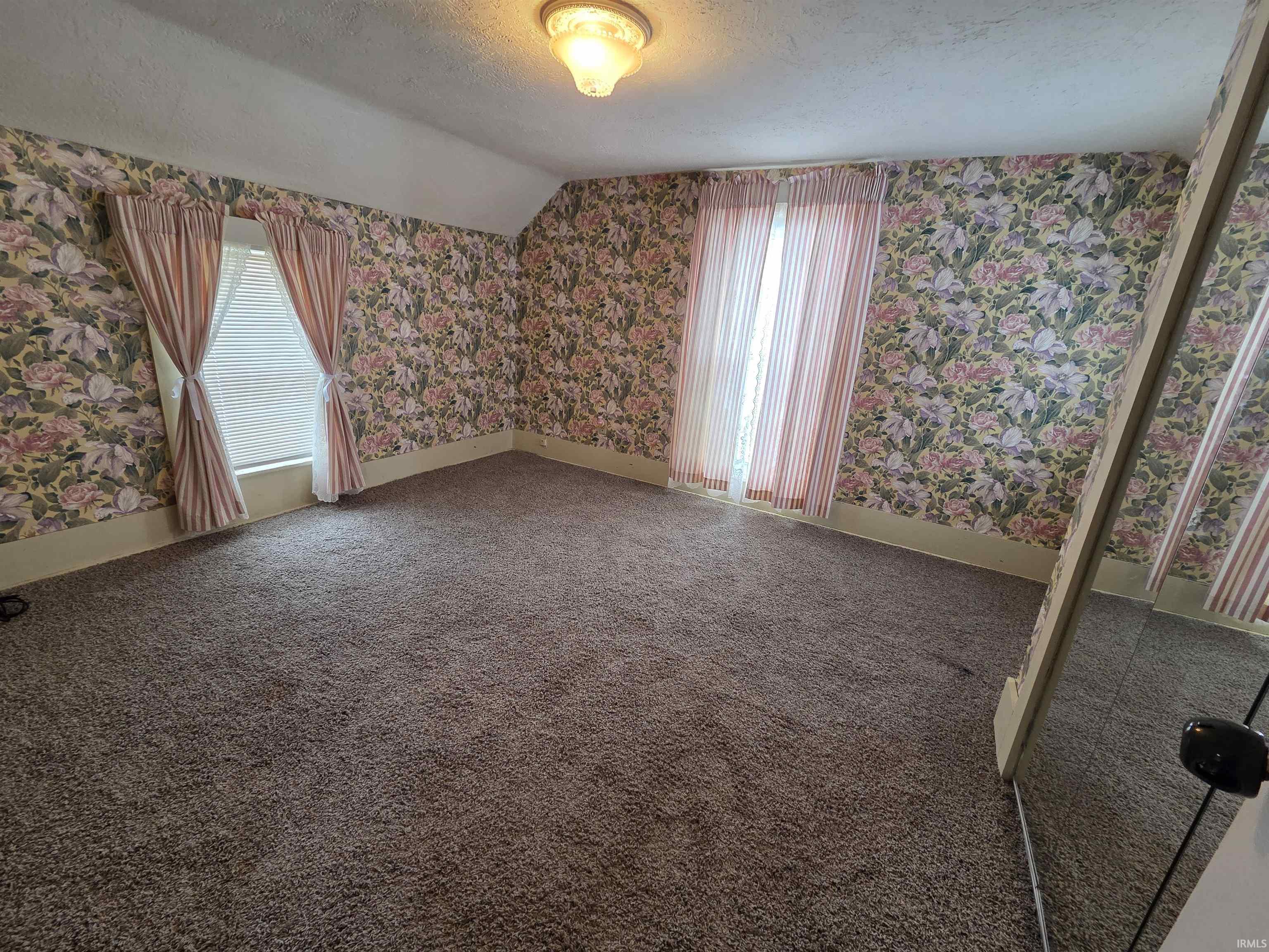 Carpeted empty room with a textured ceiling, wallpapered walls, vaulted ceiling, and plenty of natural light