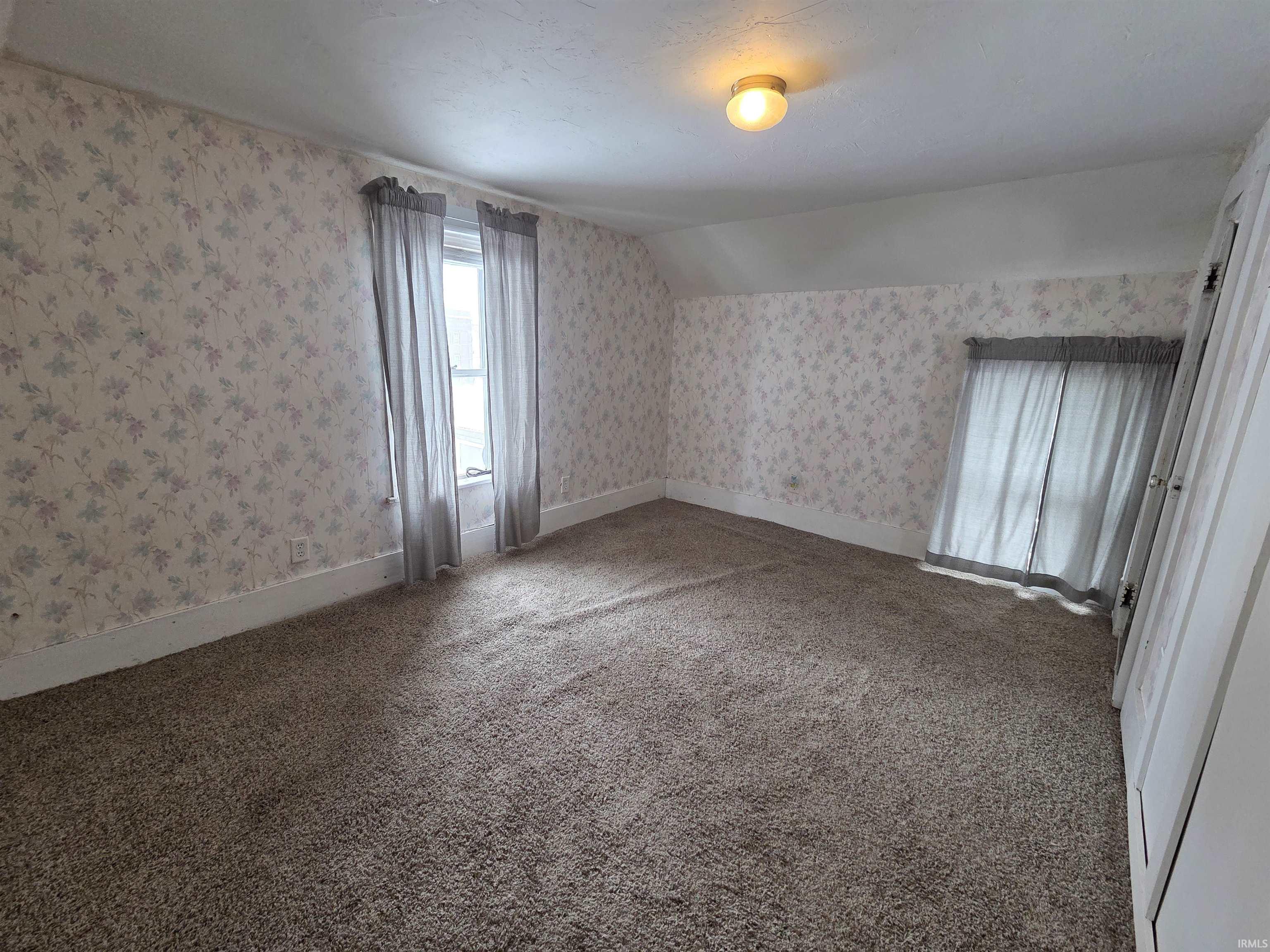 Empty room featuring wallpapered walls, vaulted ceiling, and light carpet