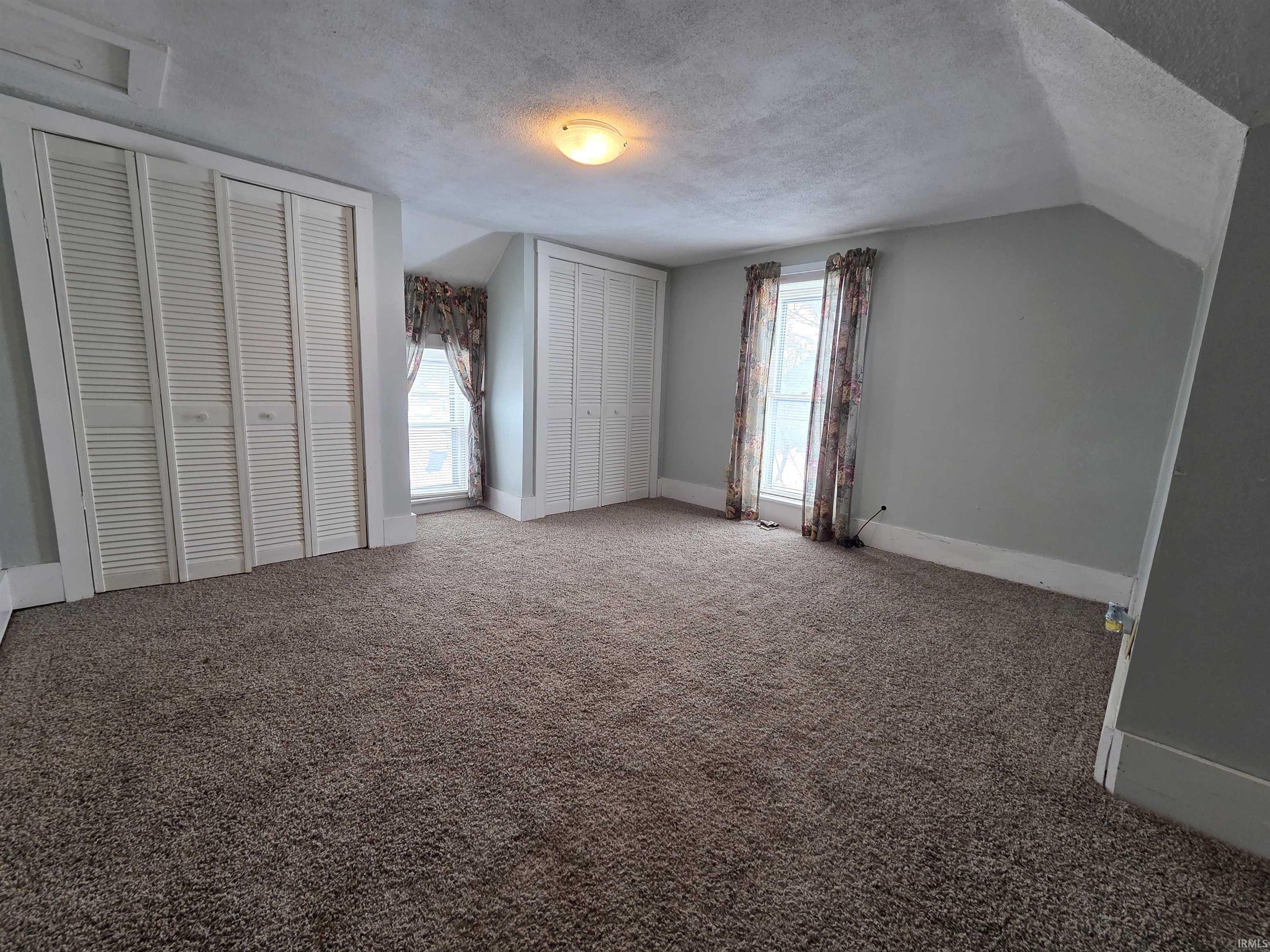 Unfurnished bedroom with a textured ceiling, two closets, carpet, and vaulted ceiling