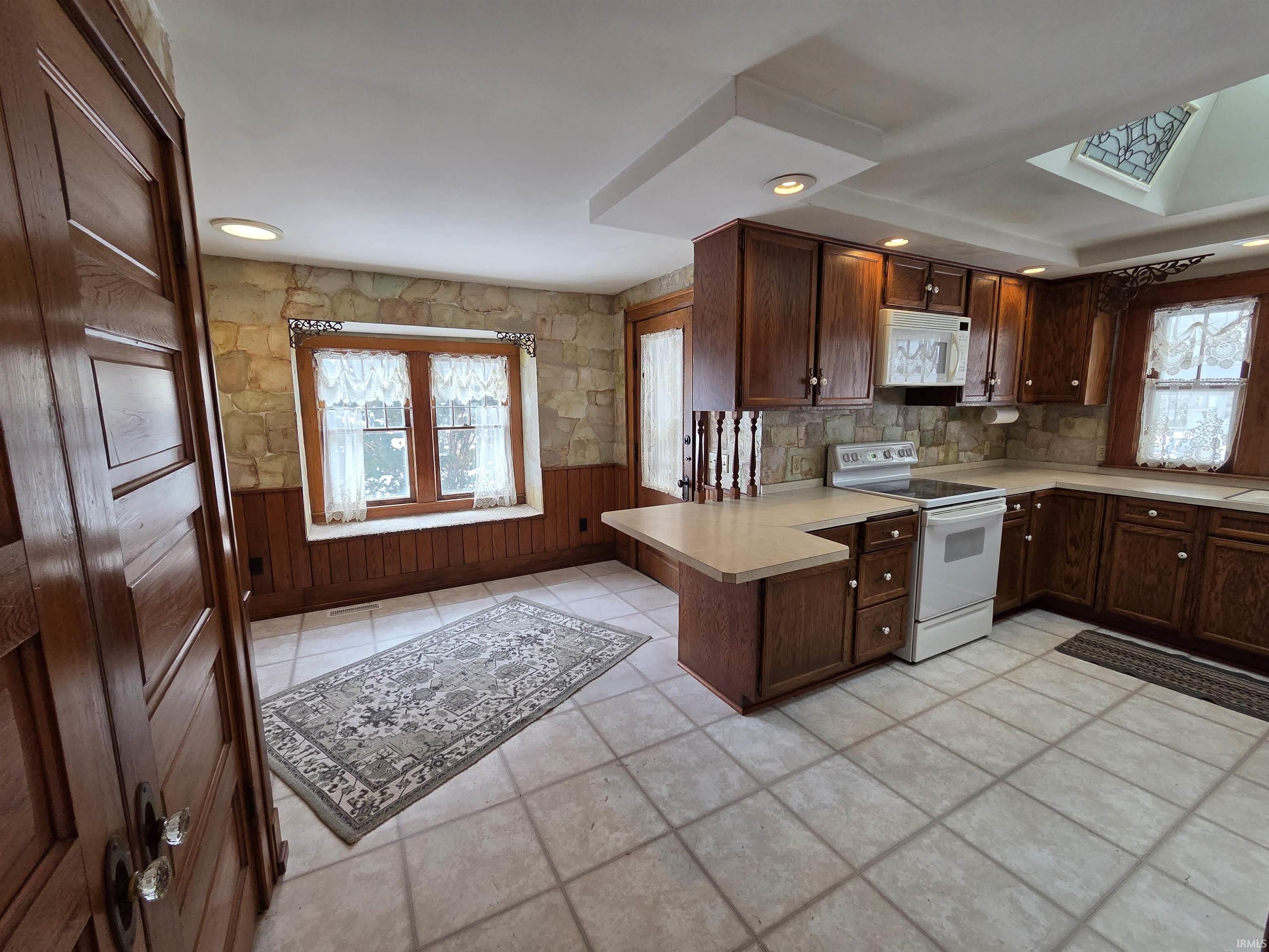 Kitchen with light countertops, white appliances, a peninsula, dark brown cabinets, and a skylight