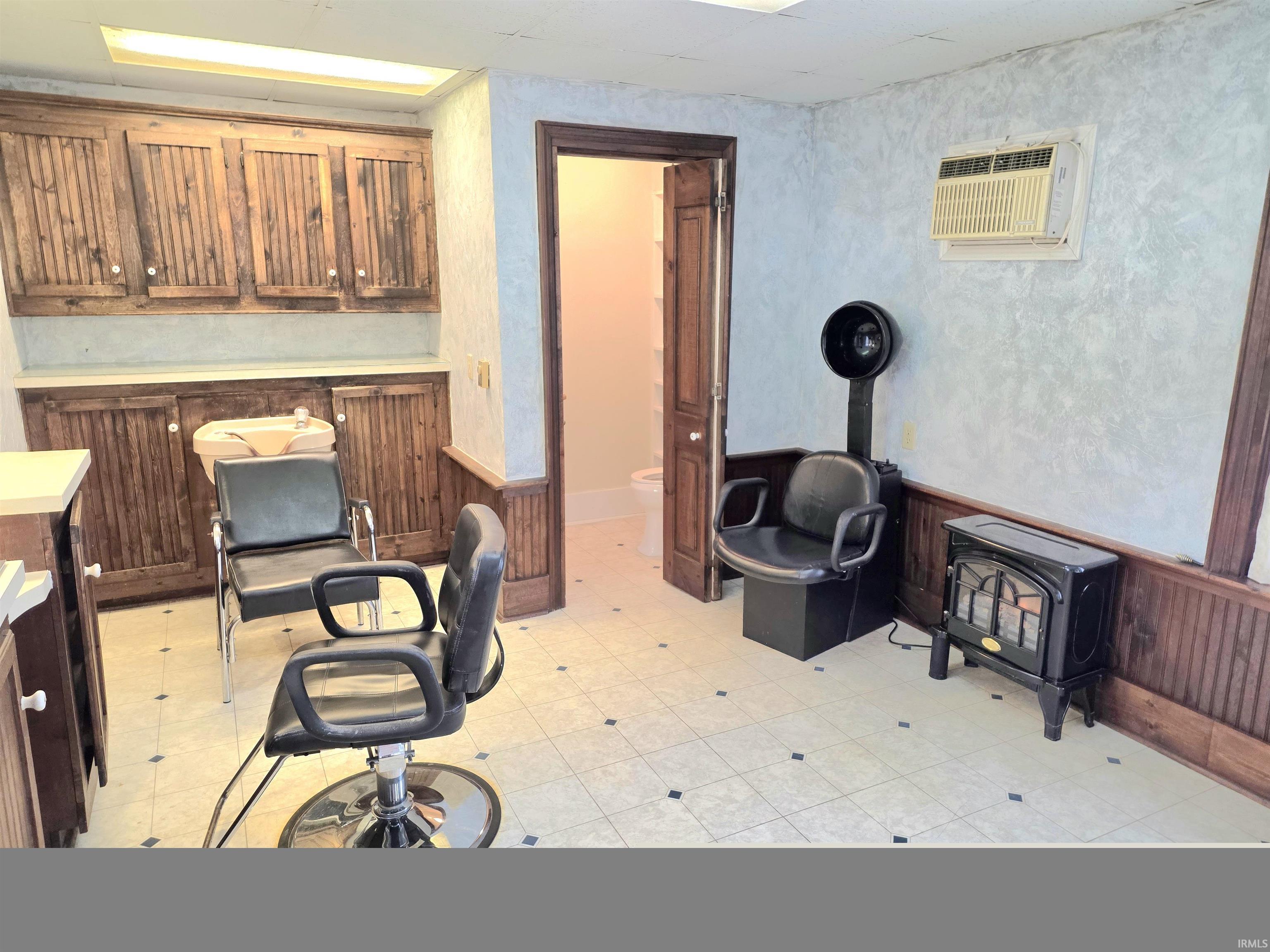 Office with wainscoting, a wood stove, wooden walls, an AC wall unit, and light flooring