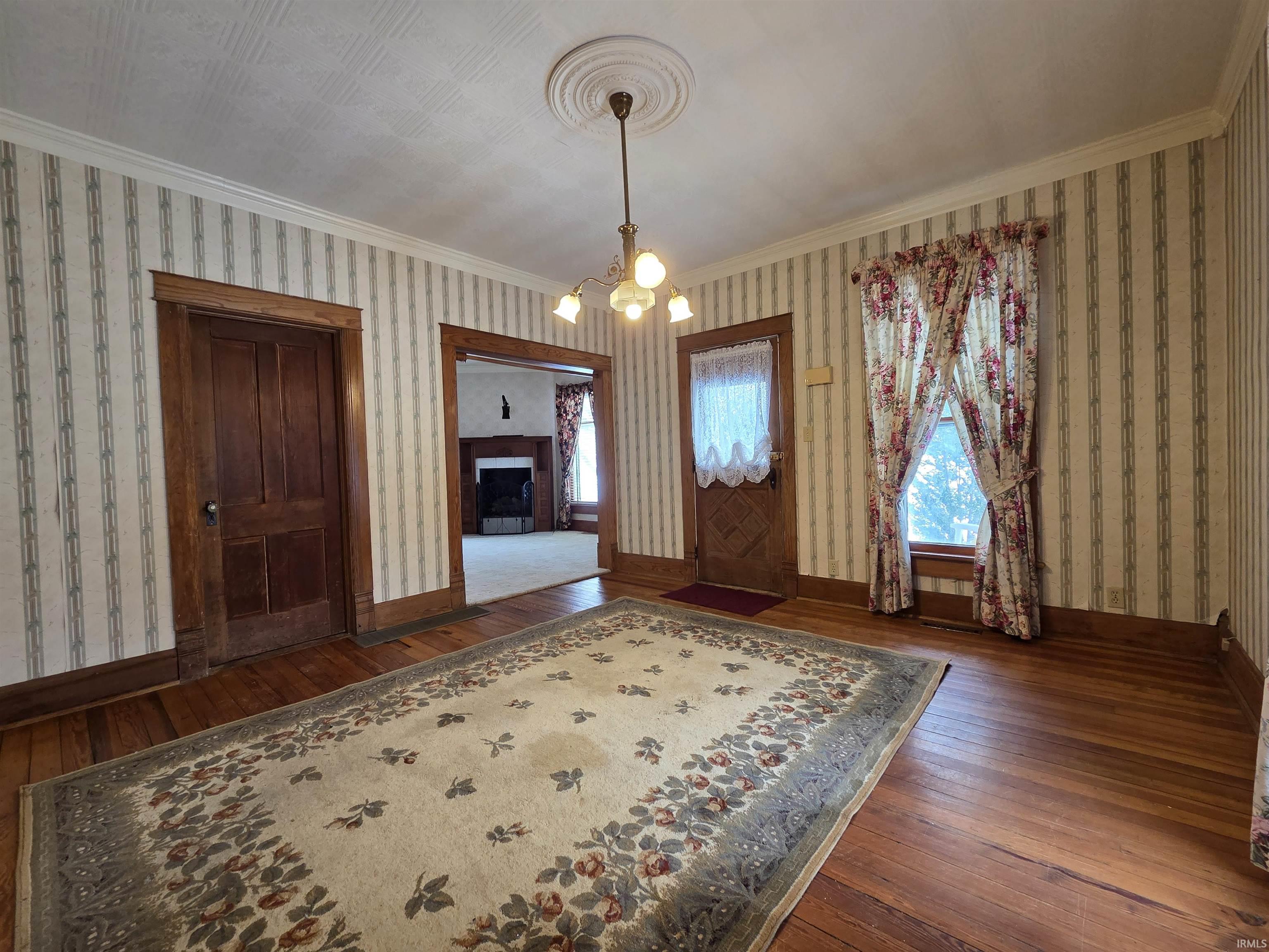 Foyer entrance featuring dark wood finished floors, crown molding, a chandelier, a fireplace, and wallpapered walls