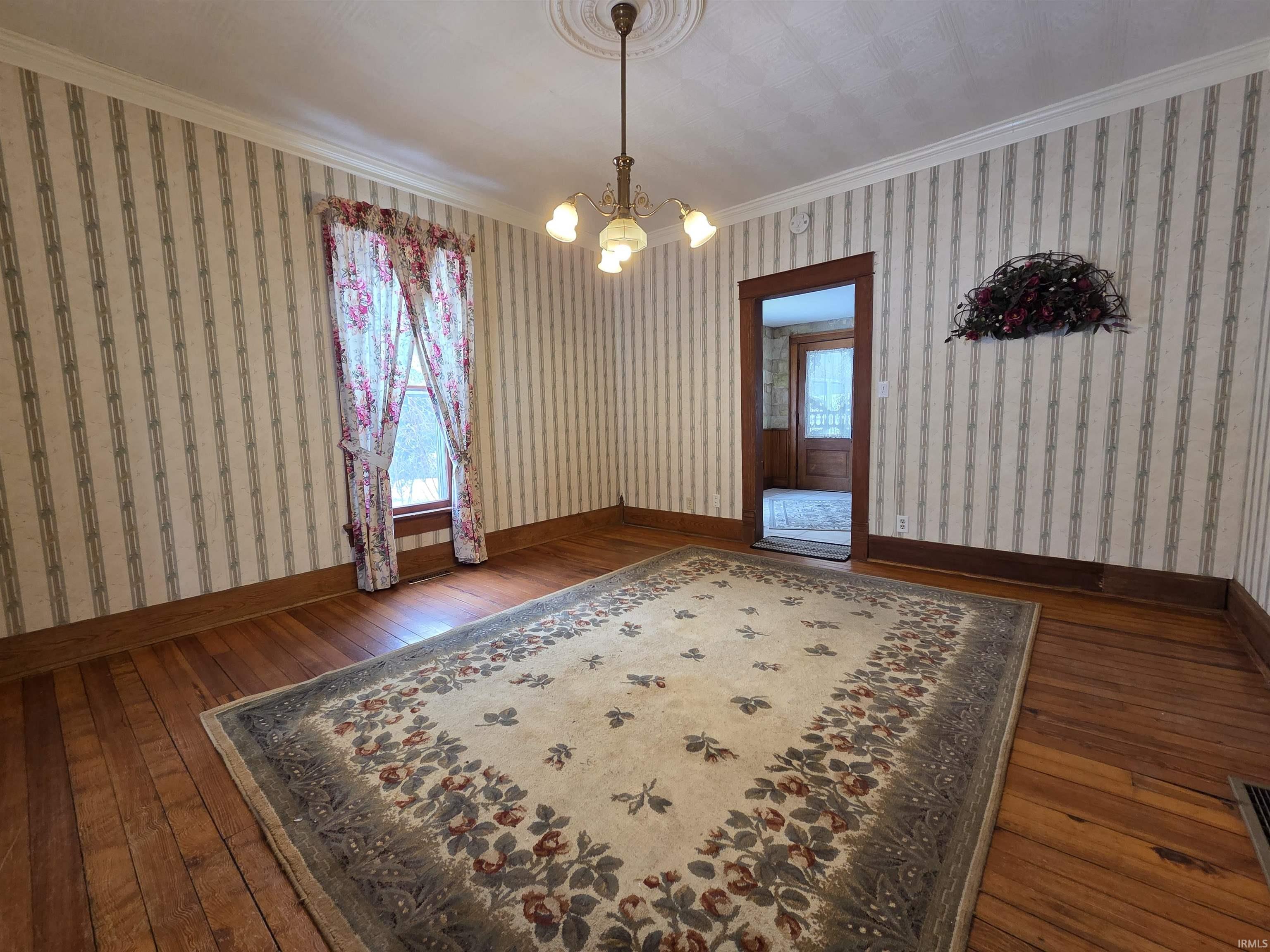 Dining room with dark wood-style flooring, ornamental molding, a chandelier, and wallpapered walls