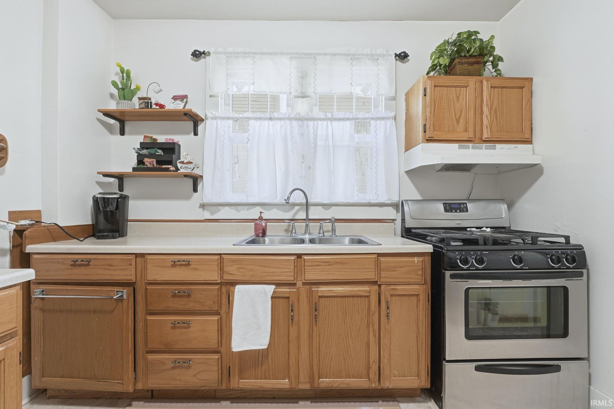 Kitchen featuring gas stove, light countertops, brown cabinetry, open shelves, and under cabinet range hood