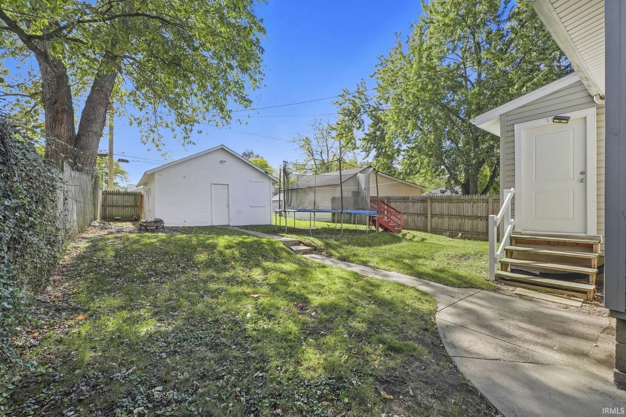 Fenced backyard with entry steps, an outbuilding, and a trampoline