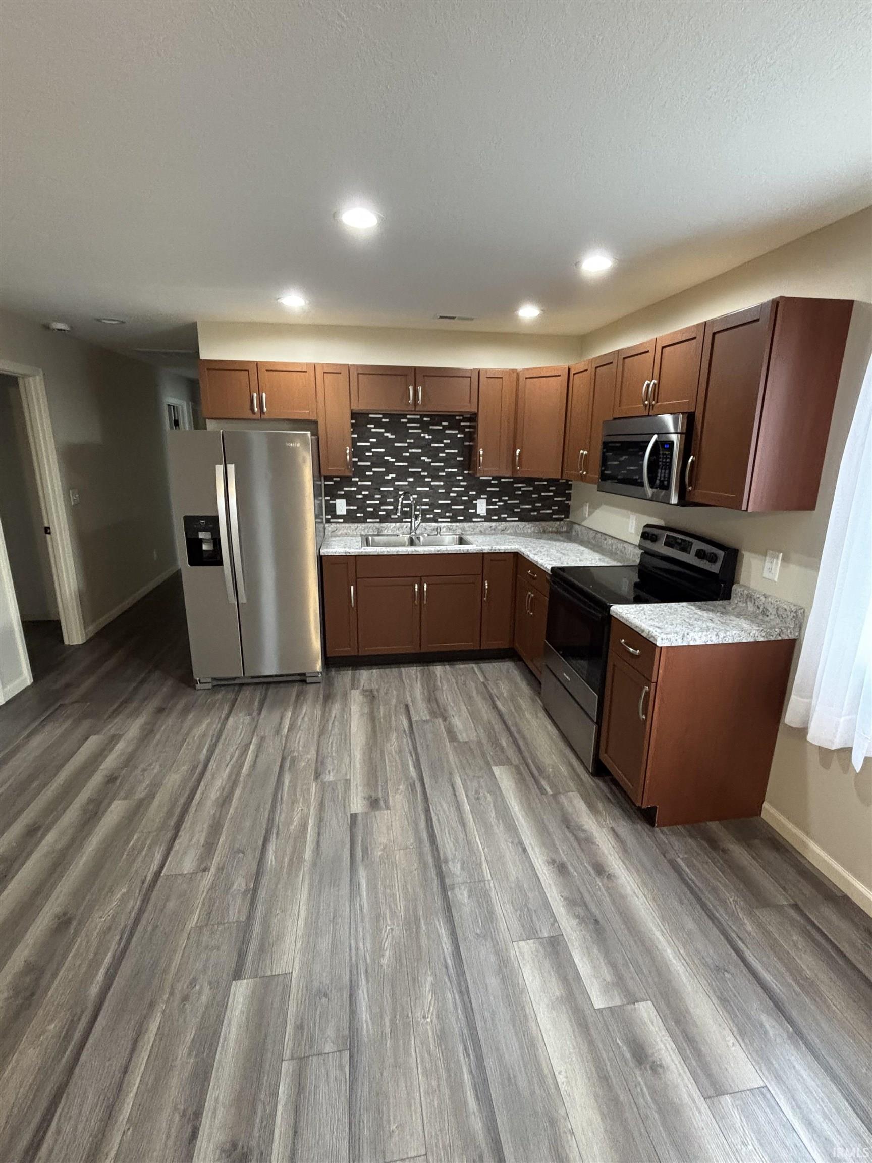 Kitchen with stainless steel appliances, light wood-style floors, light stone counters, recessed lighting, and tasteful backsplash