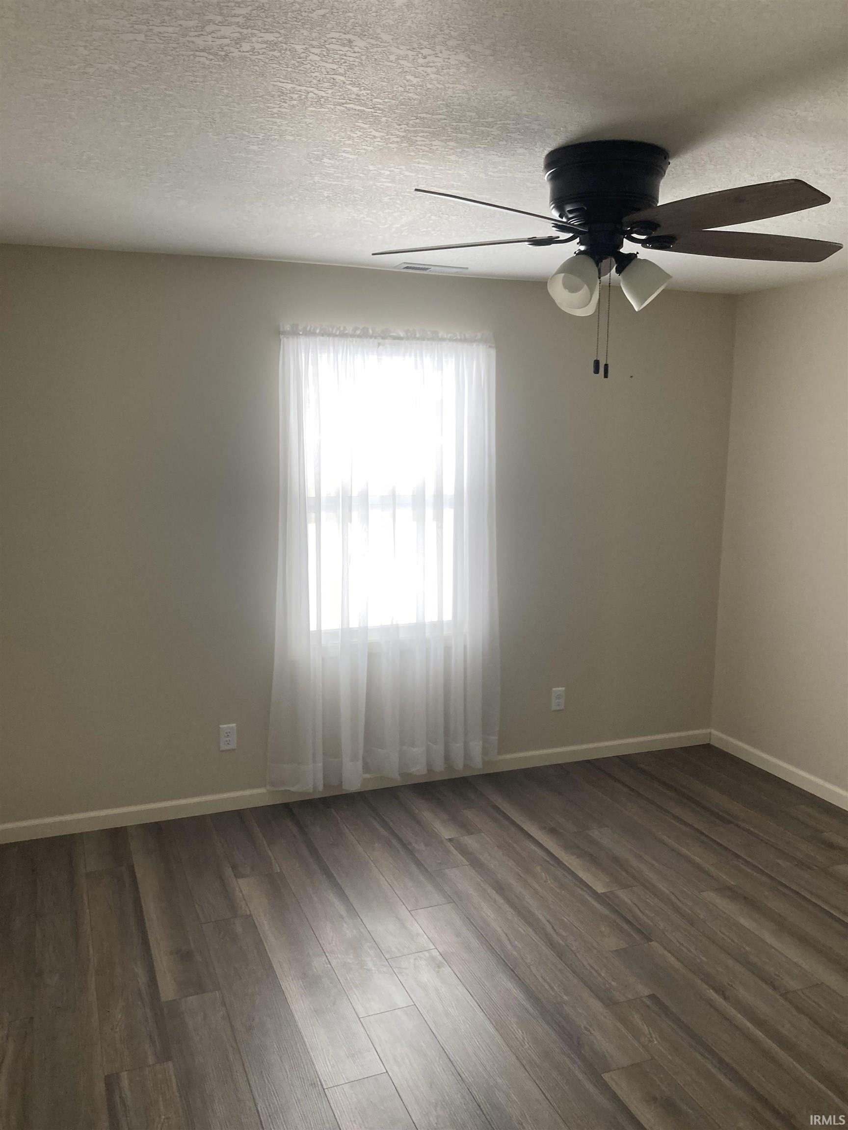 Unfurnished room featuring dark wood-style floors, a textured ceiling, and a ceiling fan