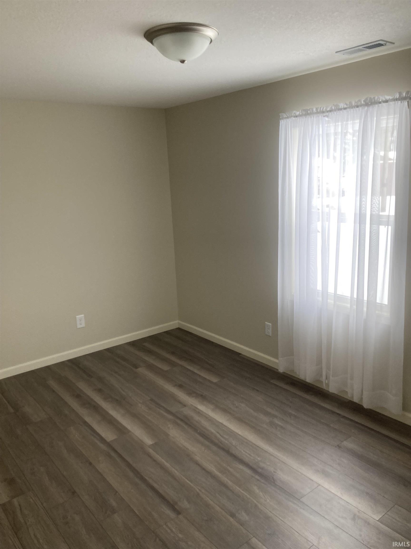 Spare room featuring dark wood-style floors and baseboards