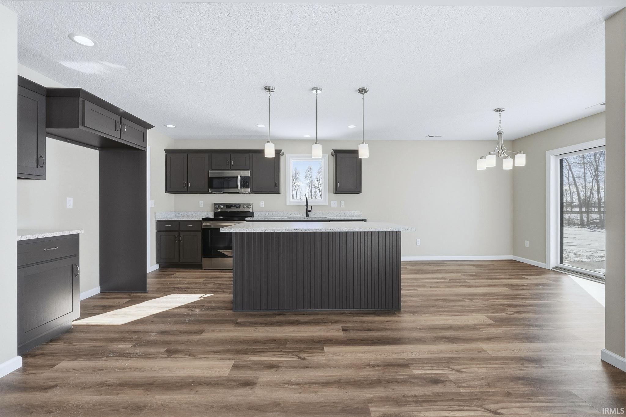 Kitchen with a kitchen island, stainless steel appliances, dark wood-type flooring, suspended lighting, and a textured ceiling