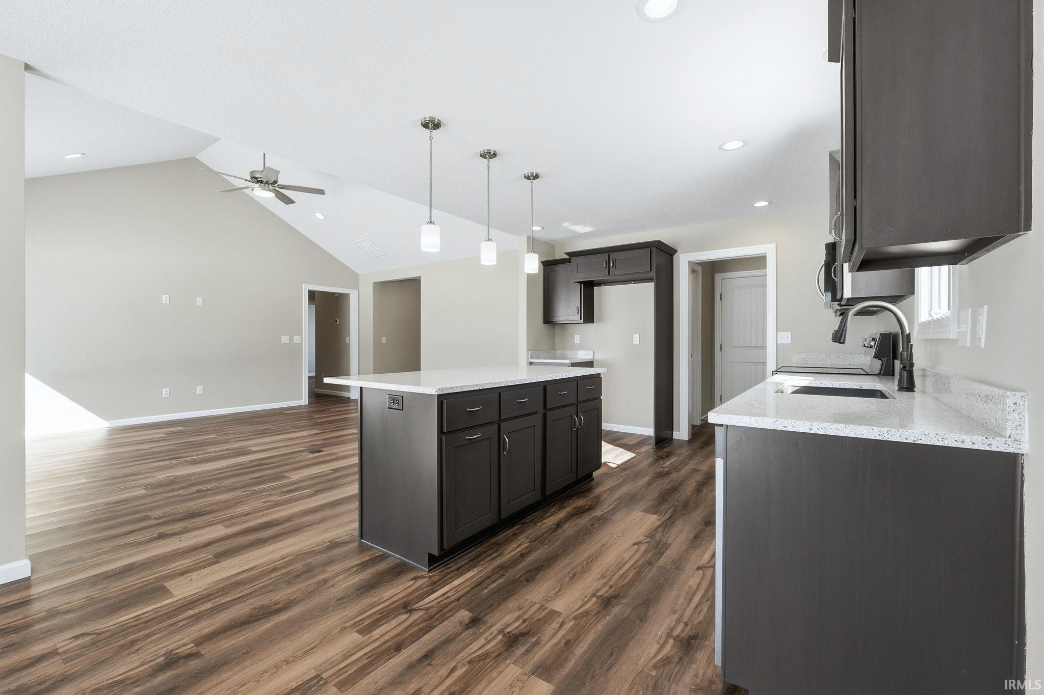 Kitchen featuring light stone counters, pendant lighting, open floor plan, ceiling fan, and a kitchen island