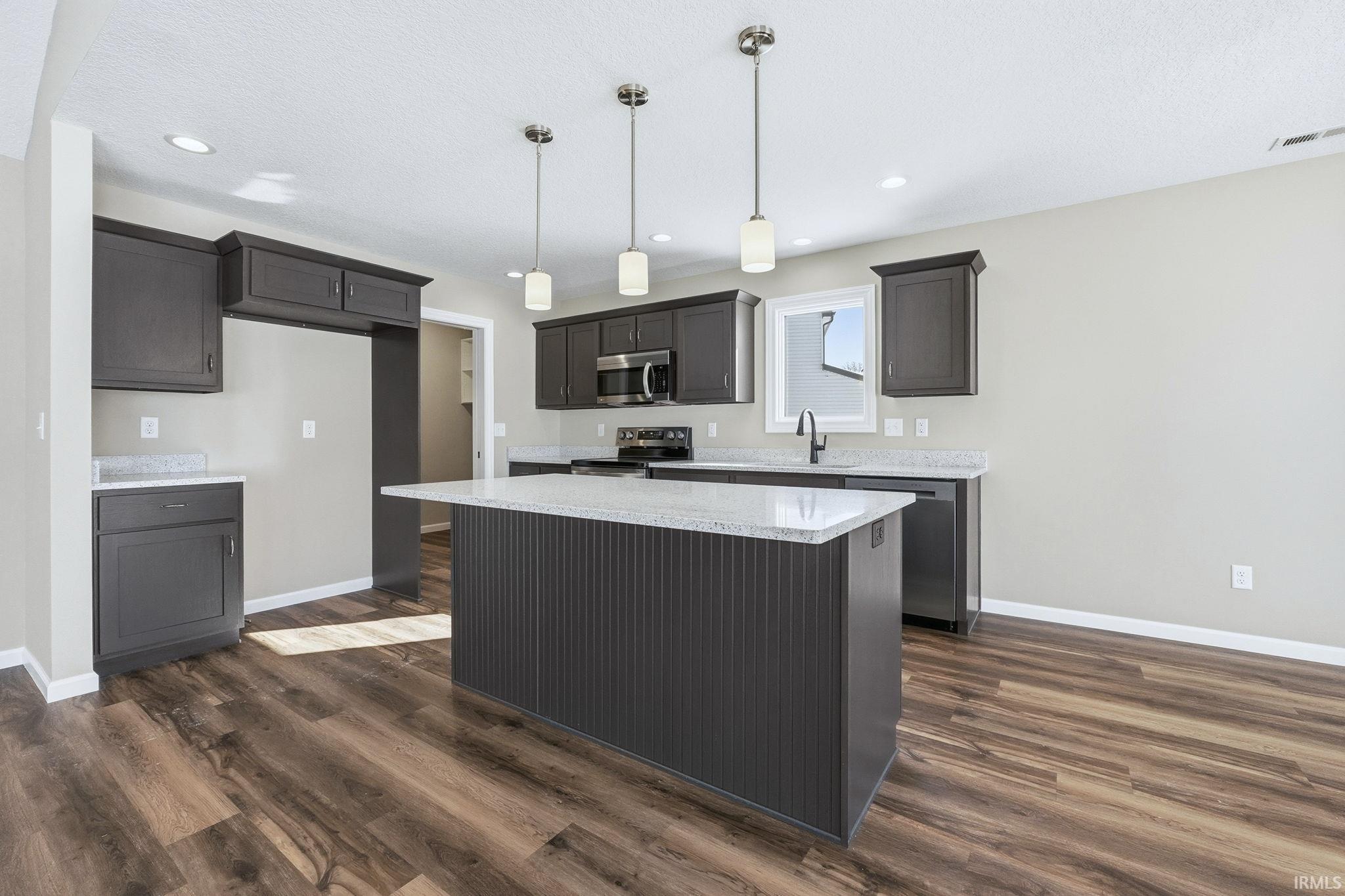 Kitchen featuring pendant lighting, light stone countertops, a center island, stainless steel appliances, and dark wood-style flooring