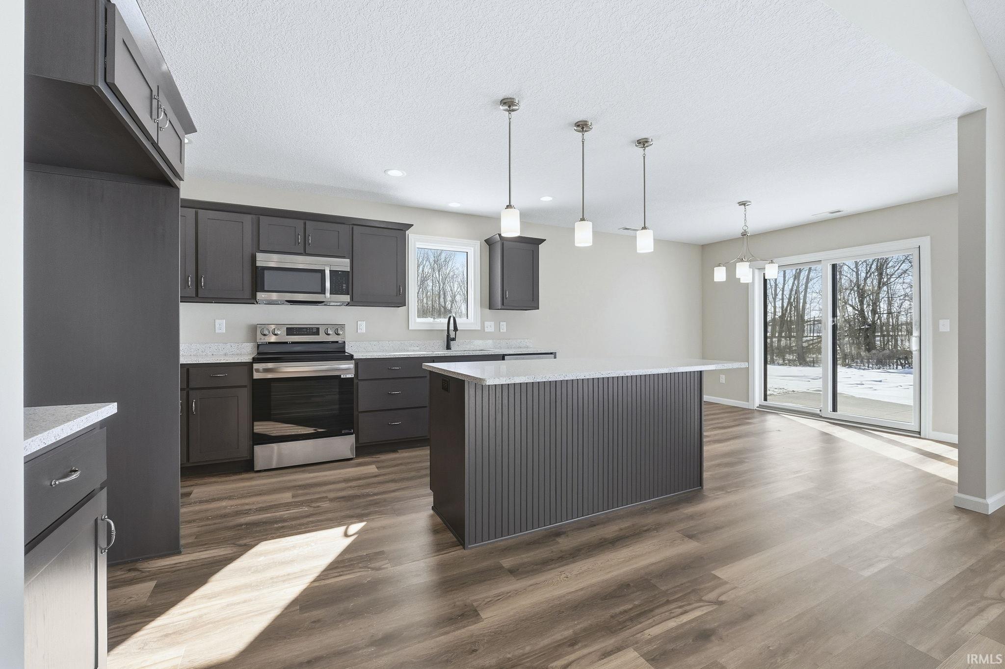 Kitchen with stainless steel appliances, decorative light fixtures, a center island, dark wood finished floors, and a textured ceiling