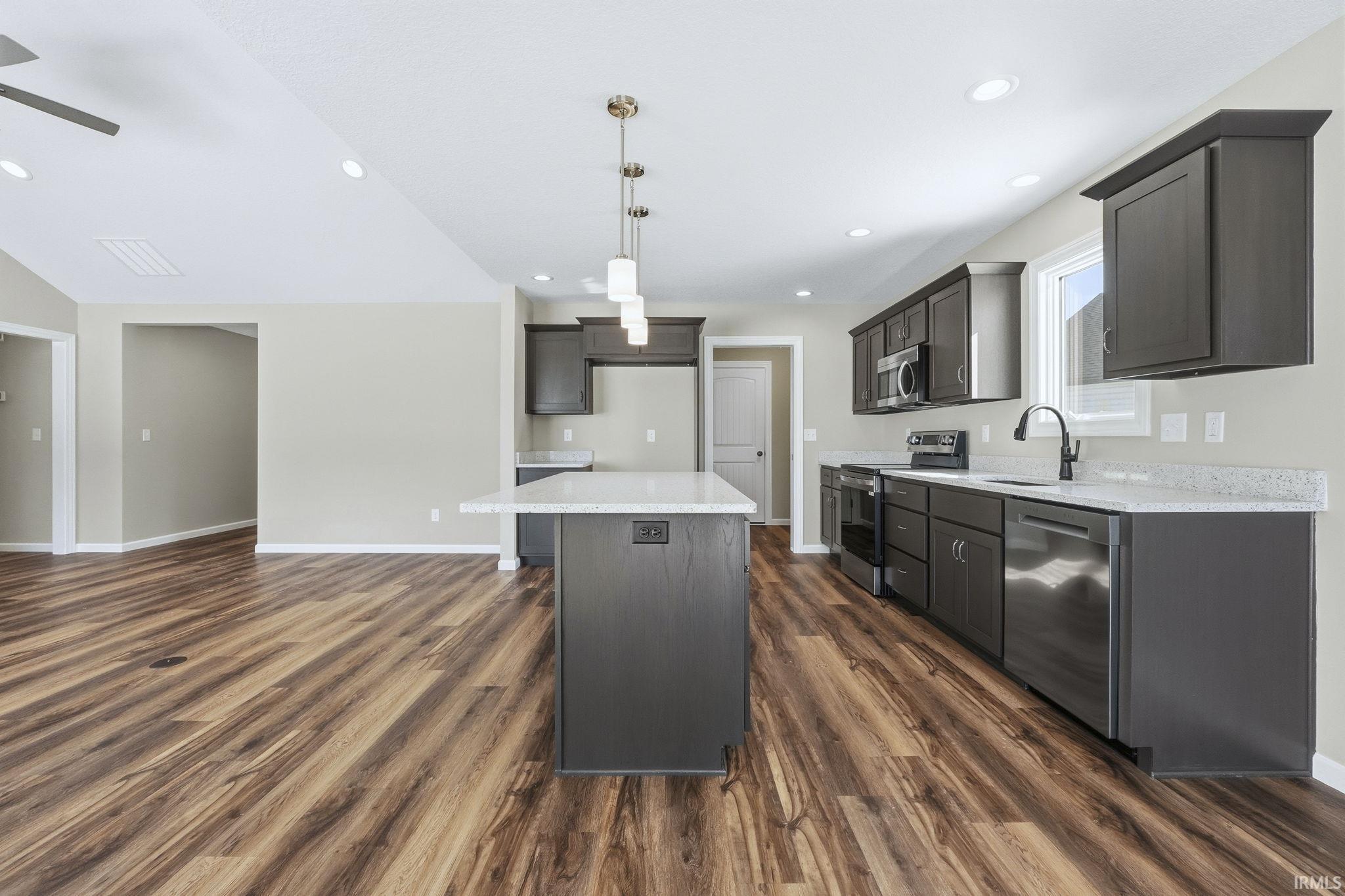 Kitchen featuring stainless steel appliances, hanging light fixtures, a center island, light stone countertops, and dark wood finished floors