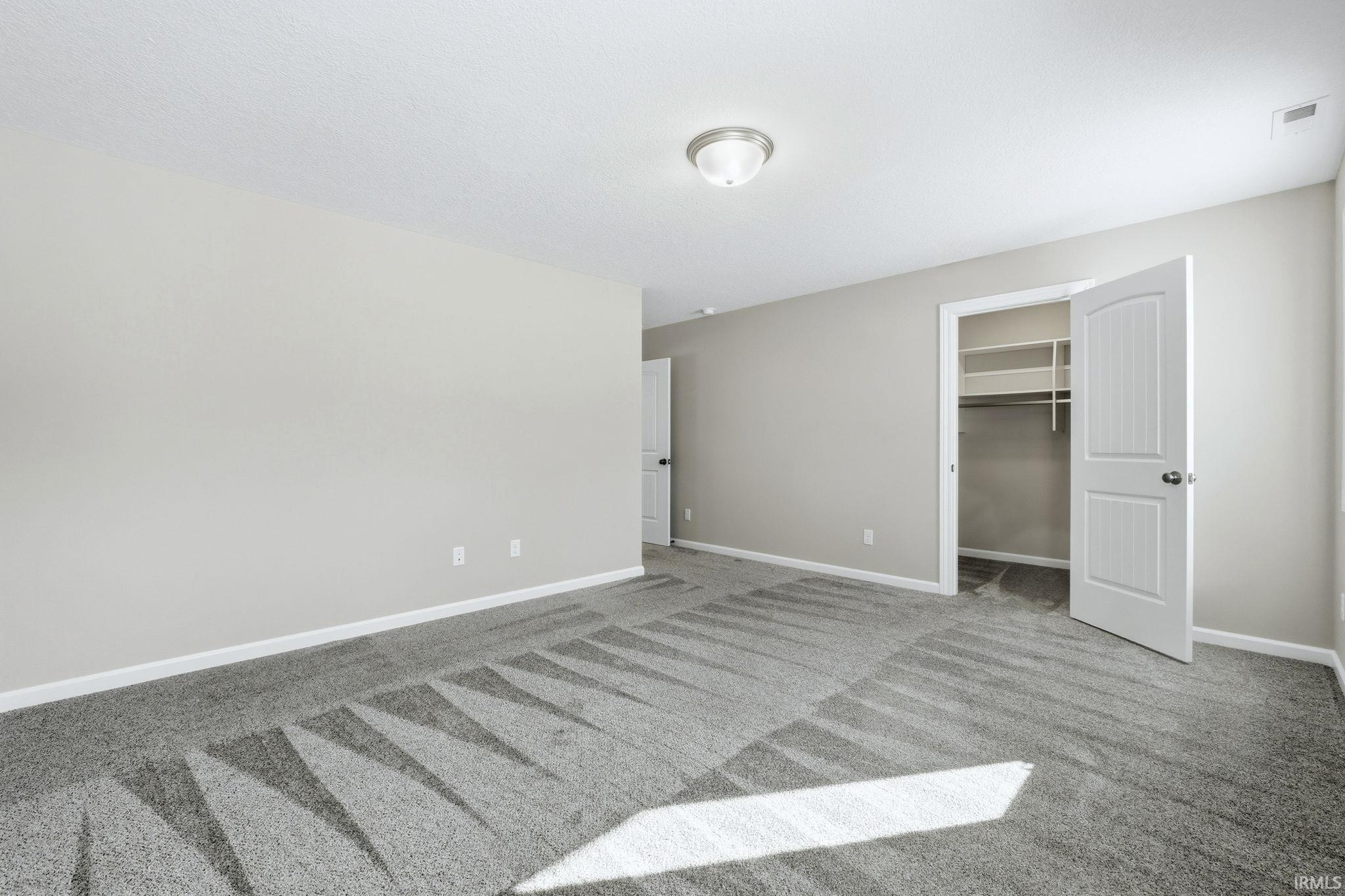 Unfurnished bedroom featuring a walk in closet and light carpet