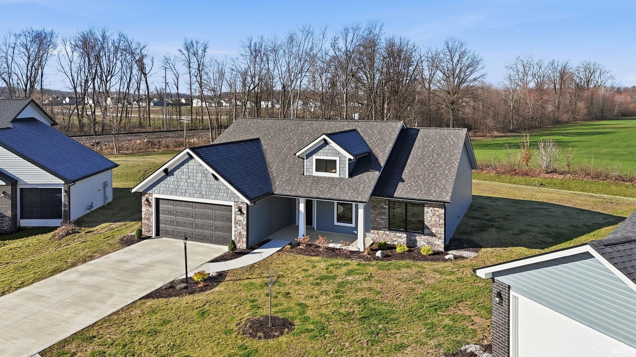 View of front of house featuring stone siding, a front yard, covered porch, roof with shingles, and driveway