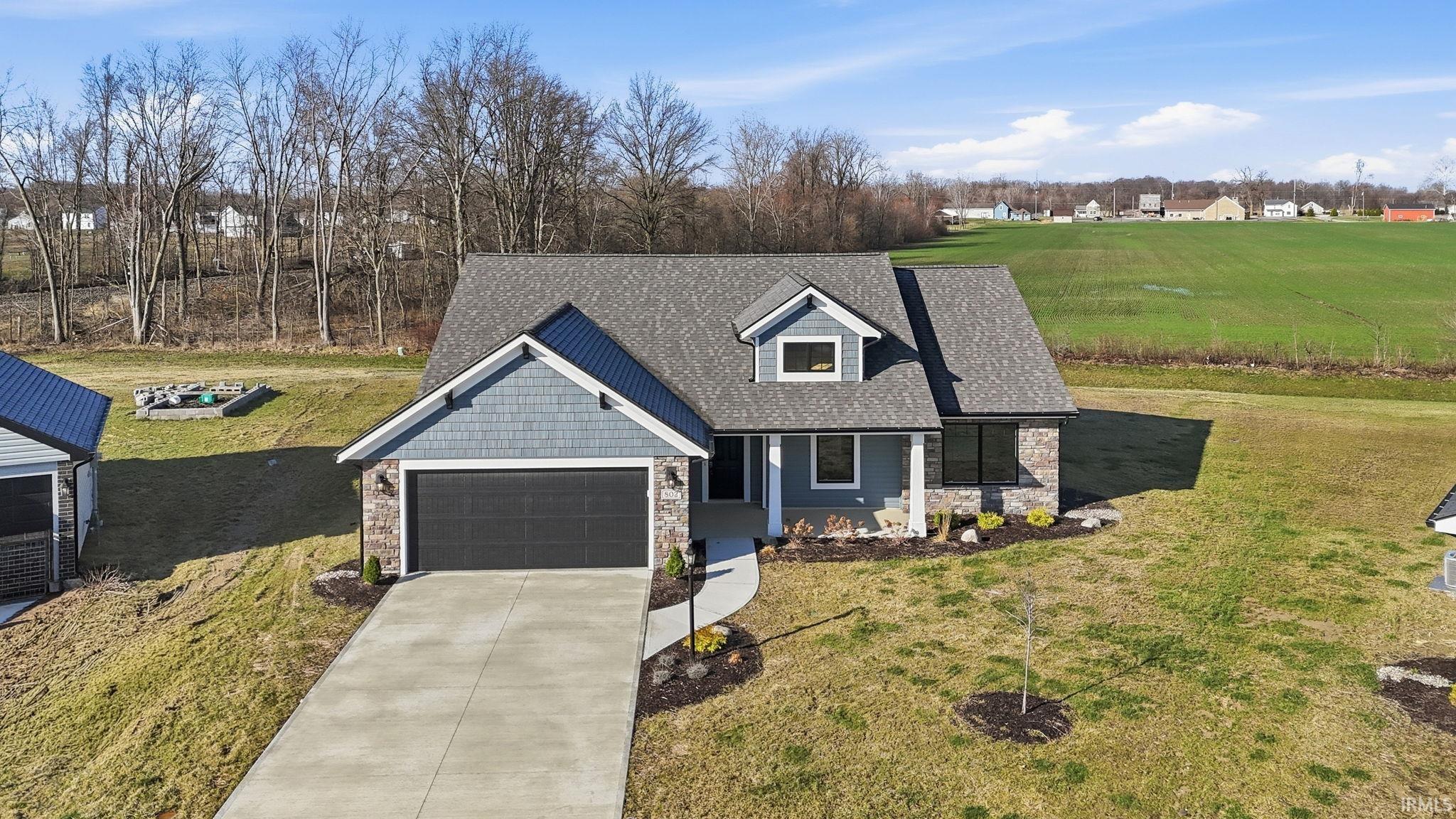 View of front of house featuring stone siding, a front lawn, driveway, a garage, and a shingled roof