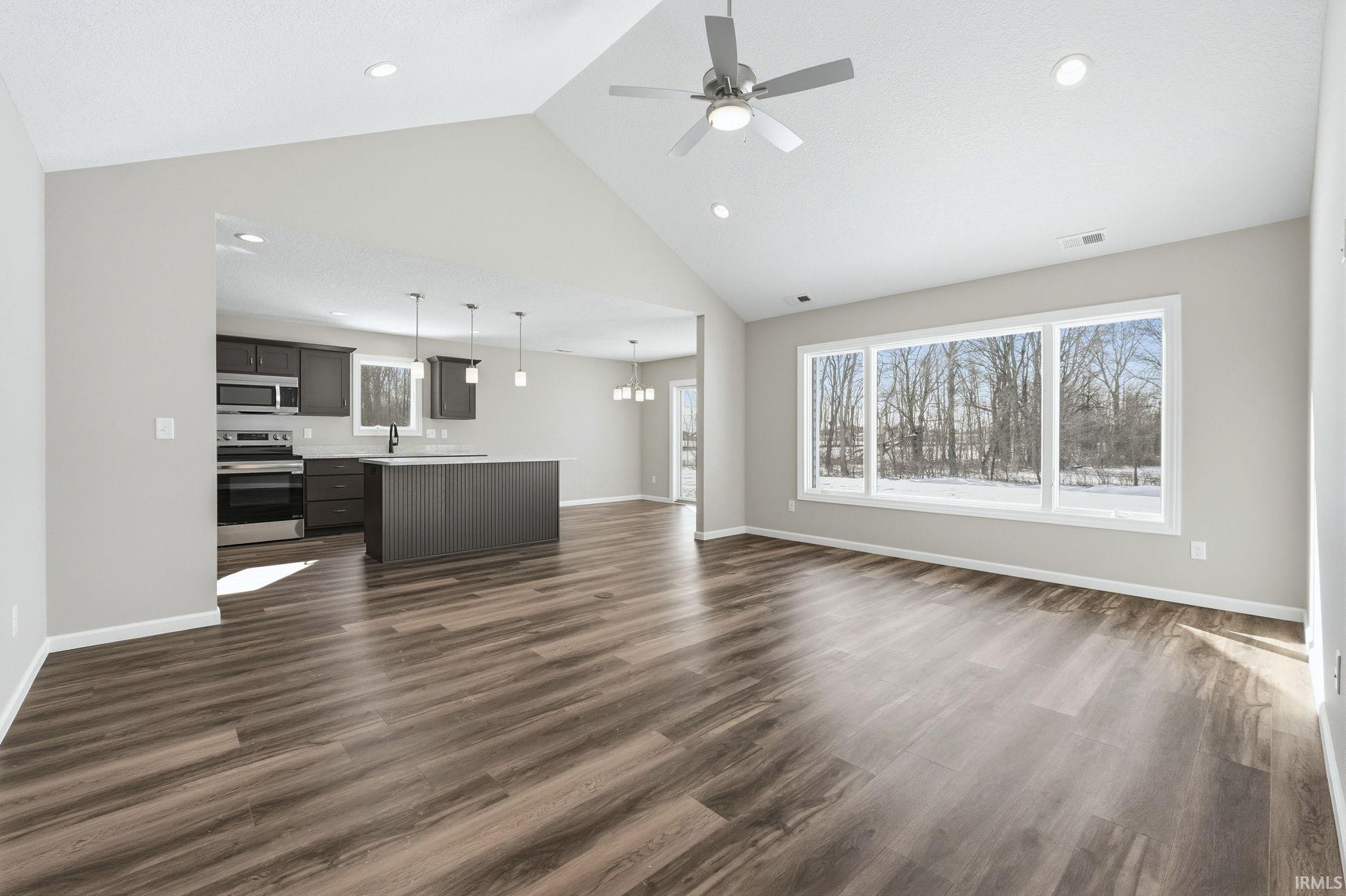 Unfurnished living room with dark wood-style floors, a ceiling fan, a high ceiling, suspended lighting, and healthy amount of natural light