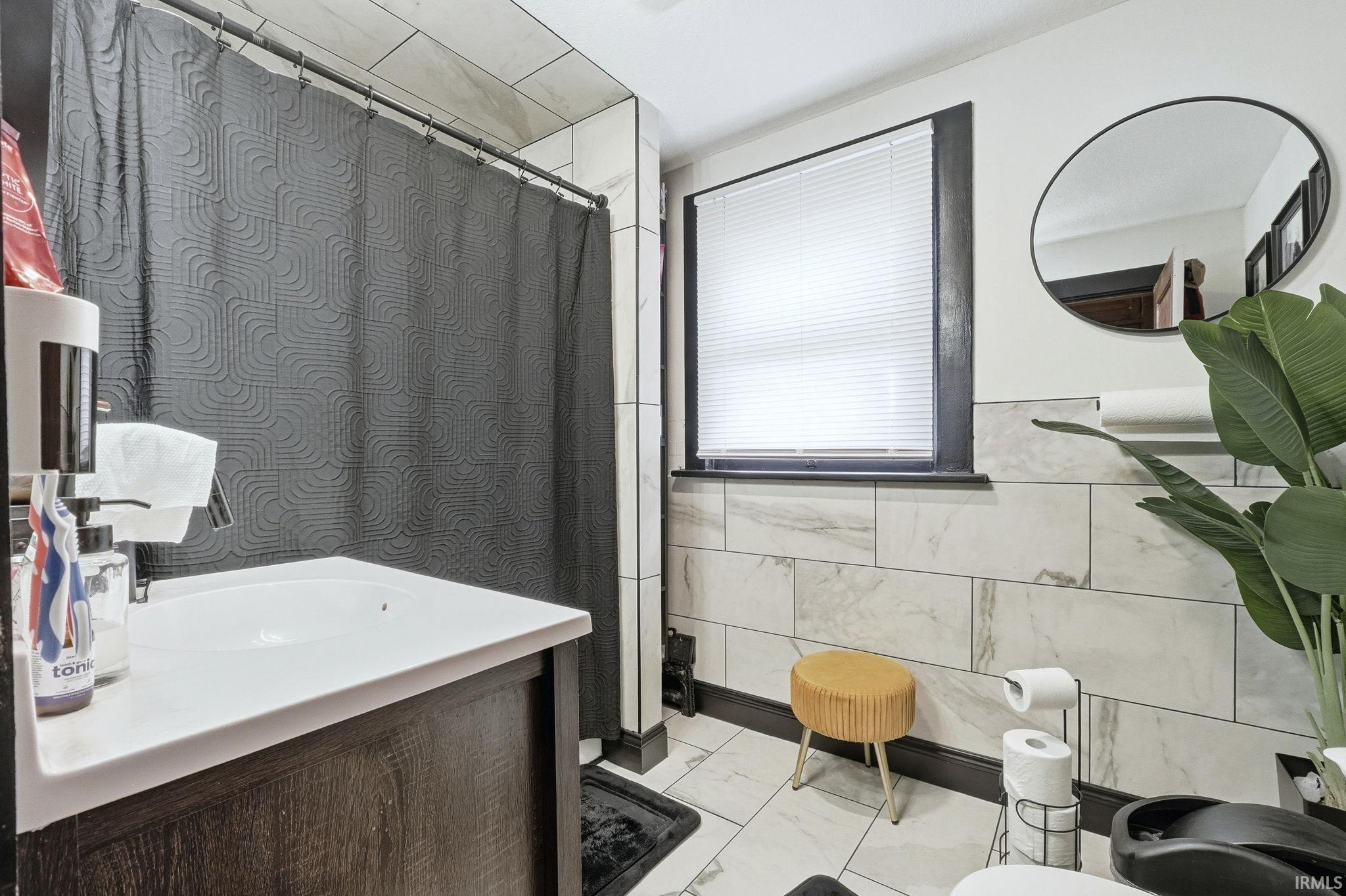 Full bathroom featuring tile walls, a shower with shower curtain, vanity, and light marble finish flooring