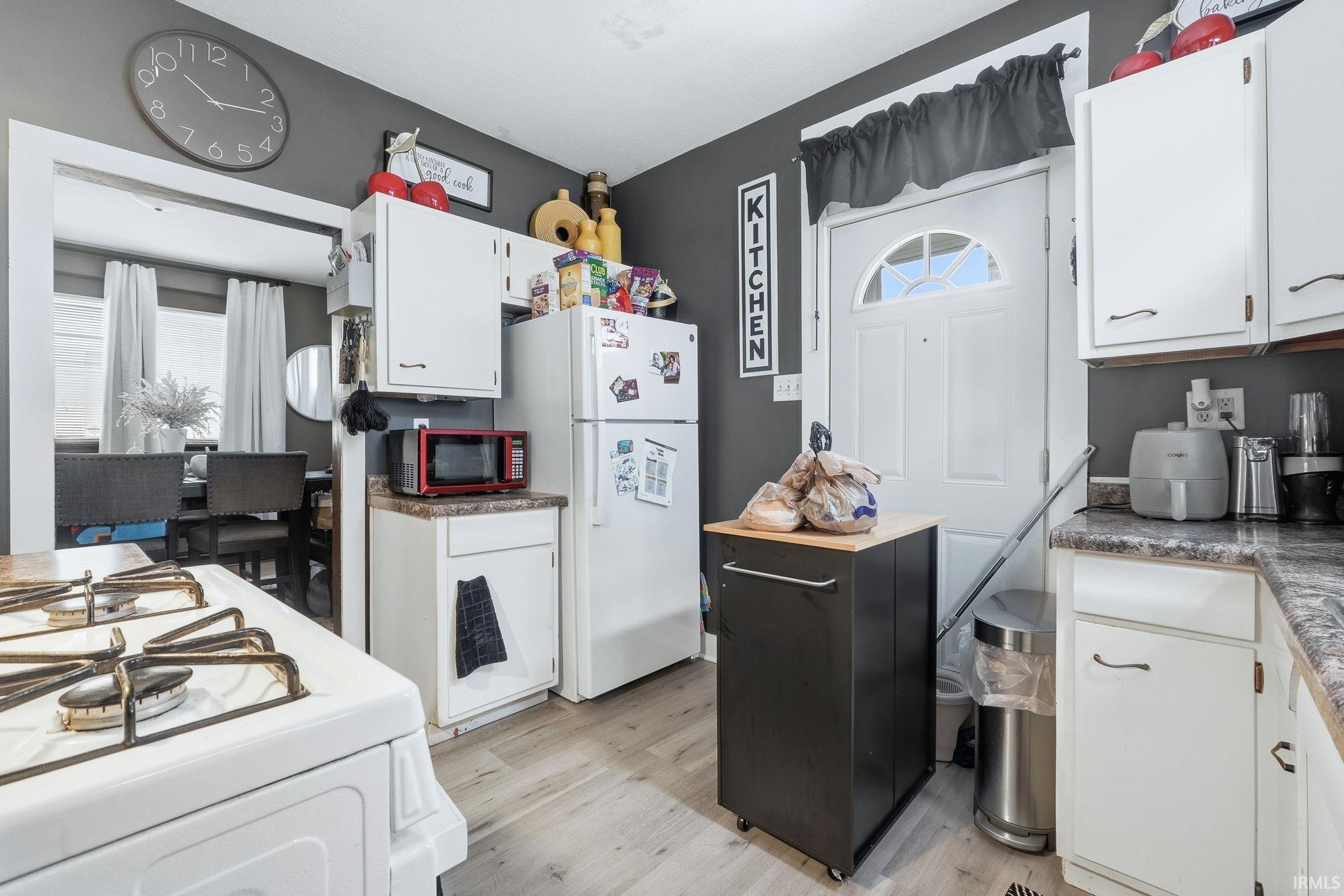 Kitchen with white cabinets, white appliances, light wood-type flooring, and dark countertops
