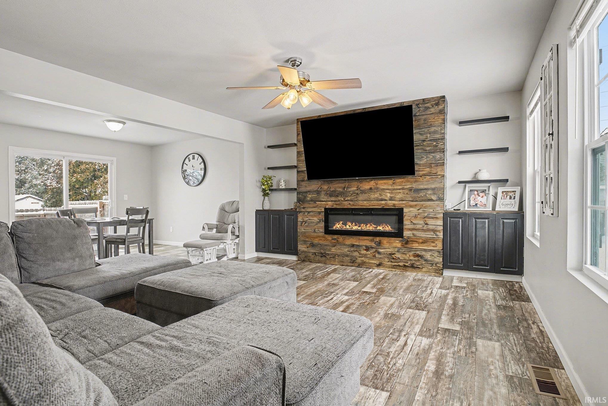 Living area with light wood finished floors, a stone fireplace, and a ceiling fan