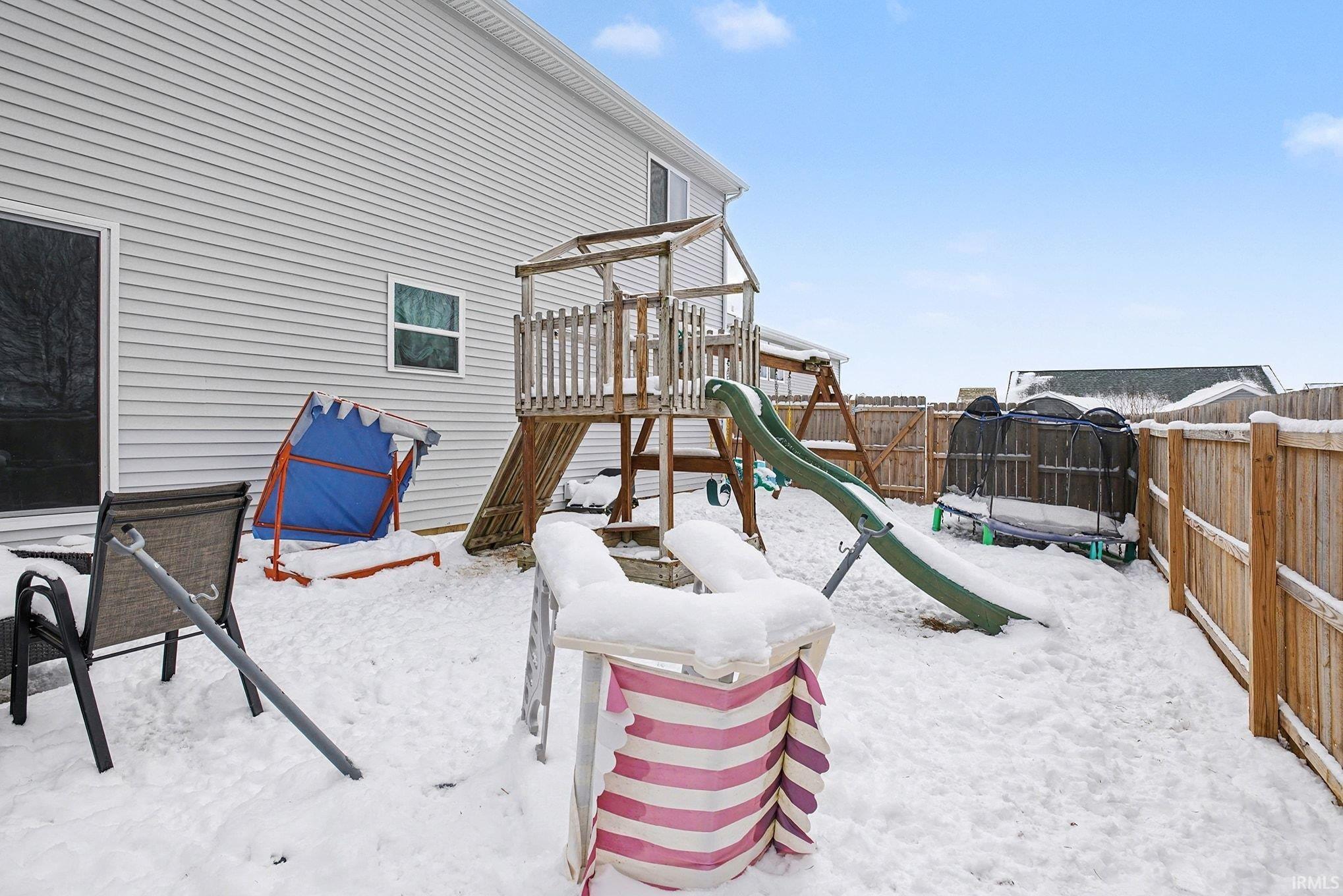 Snow covered playground with a playground and a fenced backyard