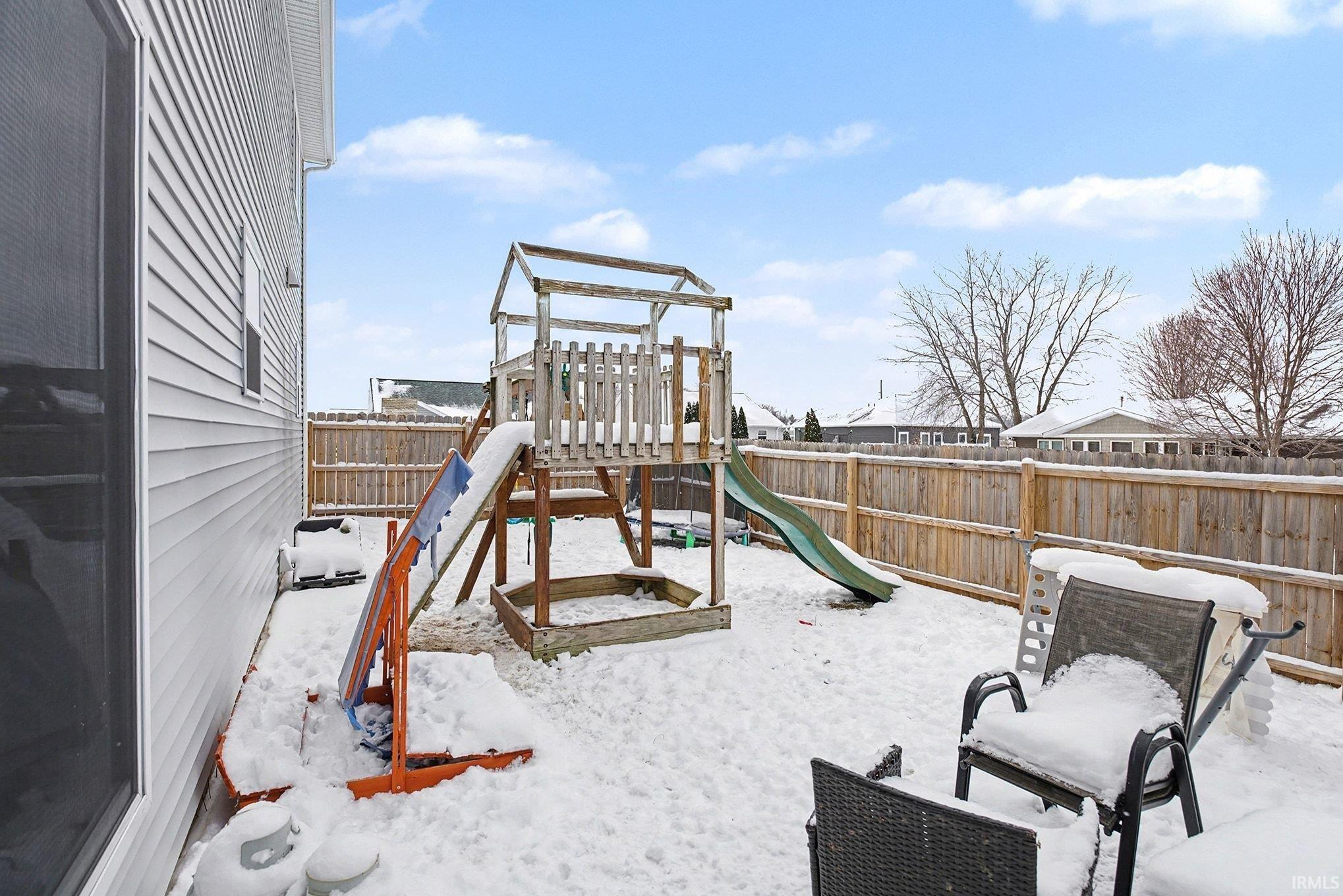Snow covered playground featuring a playground and a fenced backyard