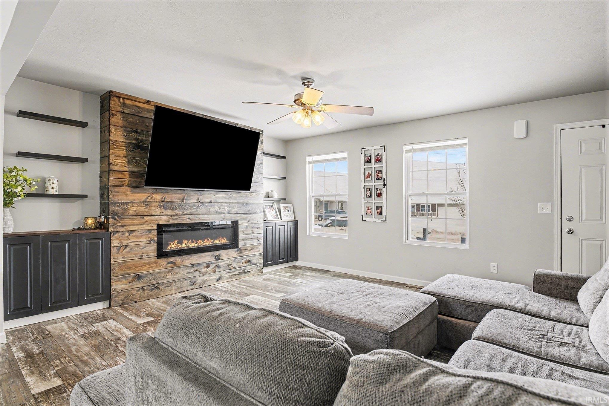 Living room with wood finished floors, a stone fireplace, and a ceiling fan