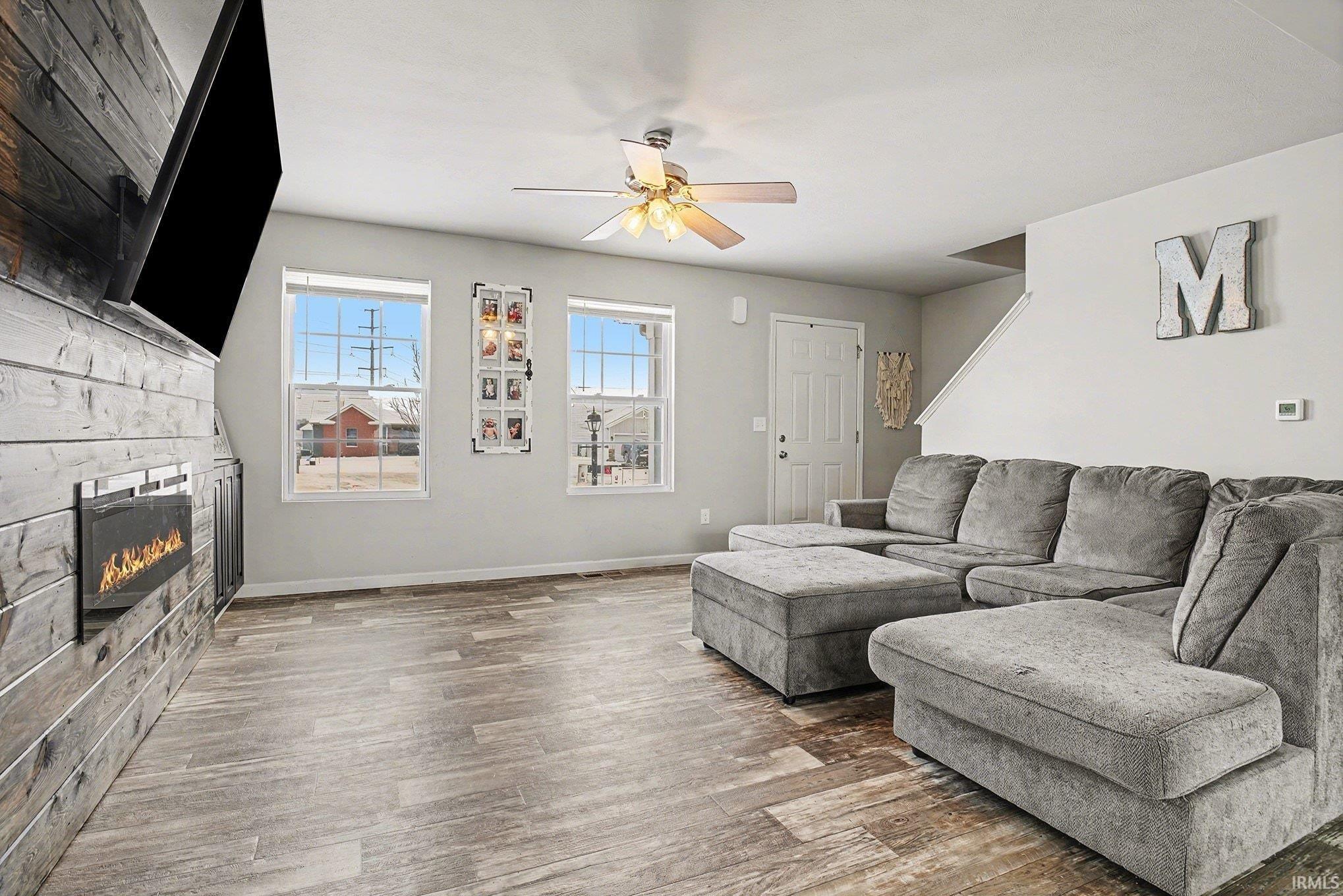 Living area featuring a stone fireplace, wood finished floors, and ceiling fan