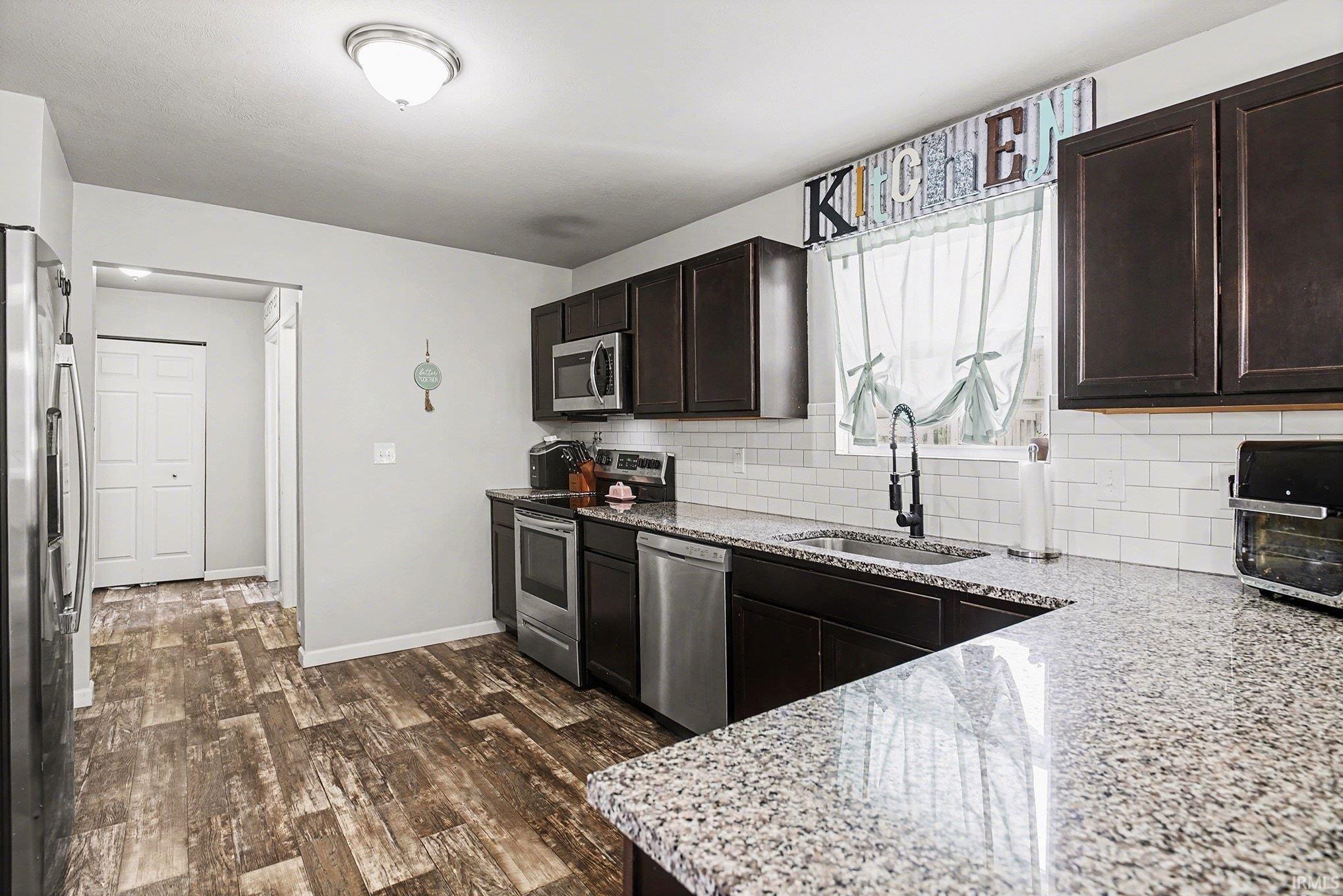 Kitchen with stainless steel appliances, light stone countertops, dark wood-style flooring, and tasteful backsplash
