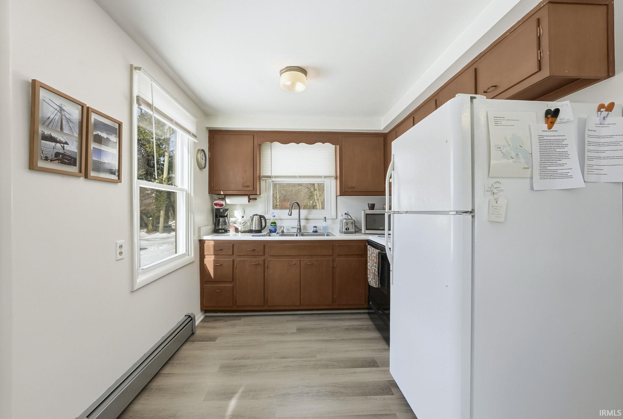 Kitchen featuring freestanding refrigerator, wood finish cabinets, baseboard heating, light countertops, and light wood-style floors