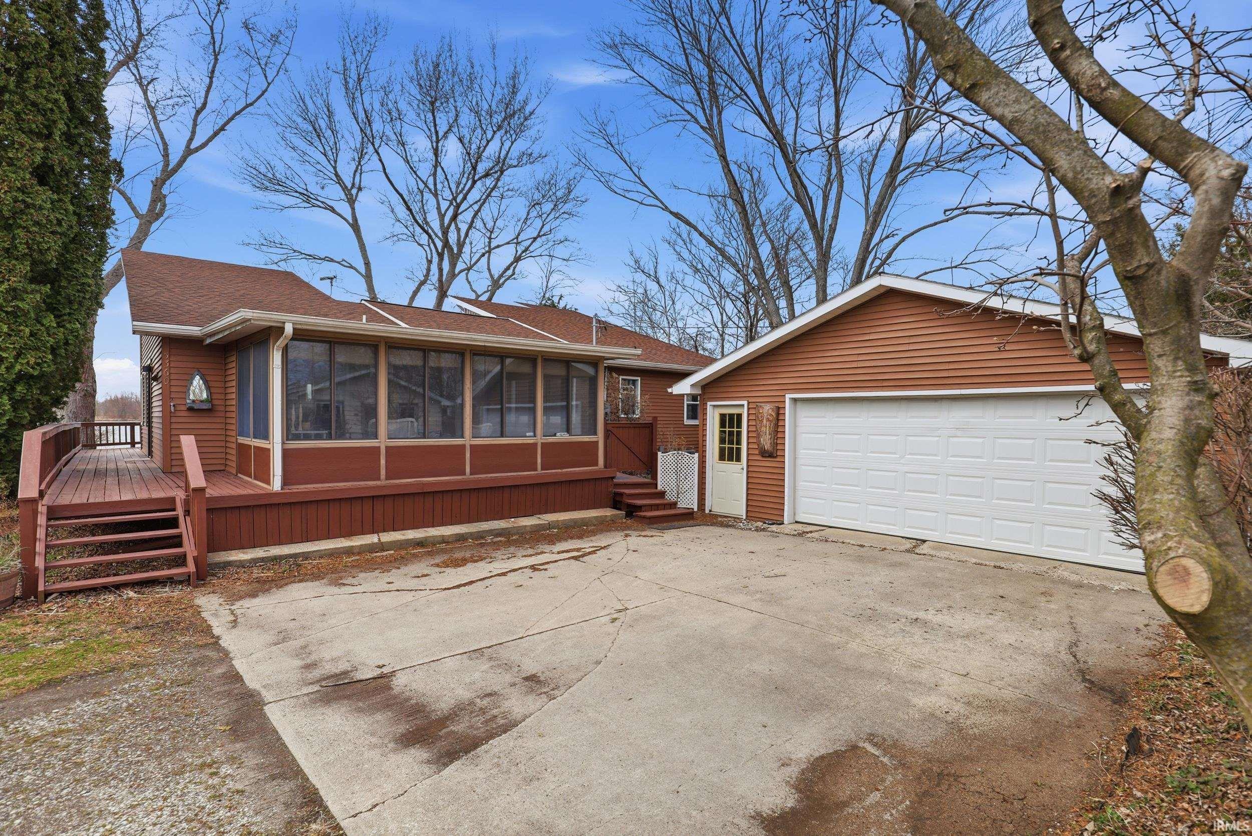 View of front of house with a sunroom, a deck, a detached garage, roof with shingles, and an outbuilding