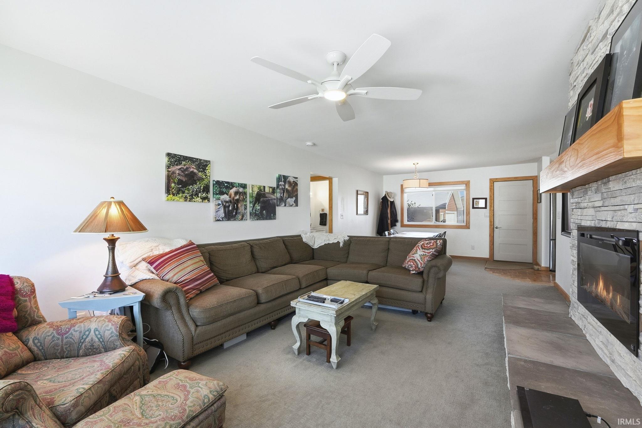 Living room featuring carpet floors, a stone fireplace, and a ceiling fan