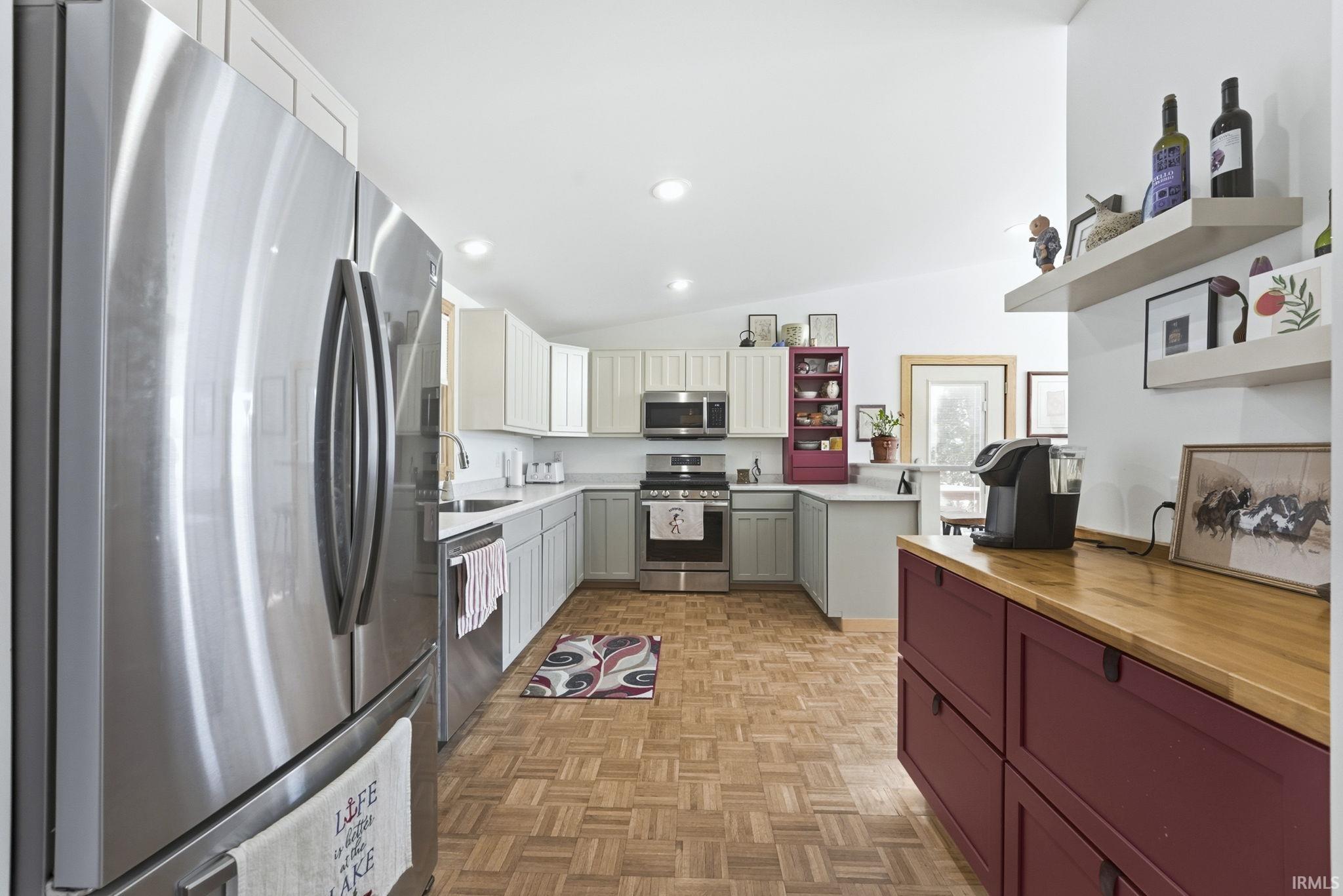 Kitchen with dual tone cabinetry, open shelves, stainless steel appliances, lofted ceiling, and parquet floors