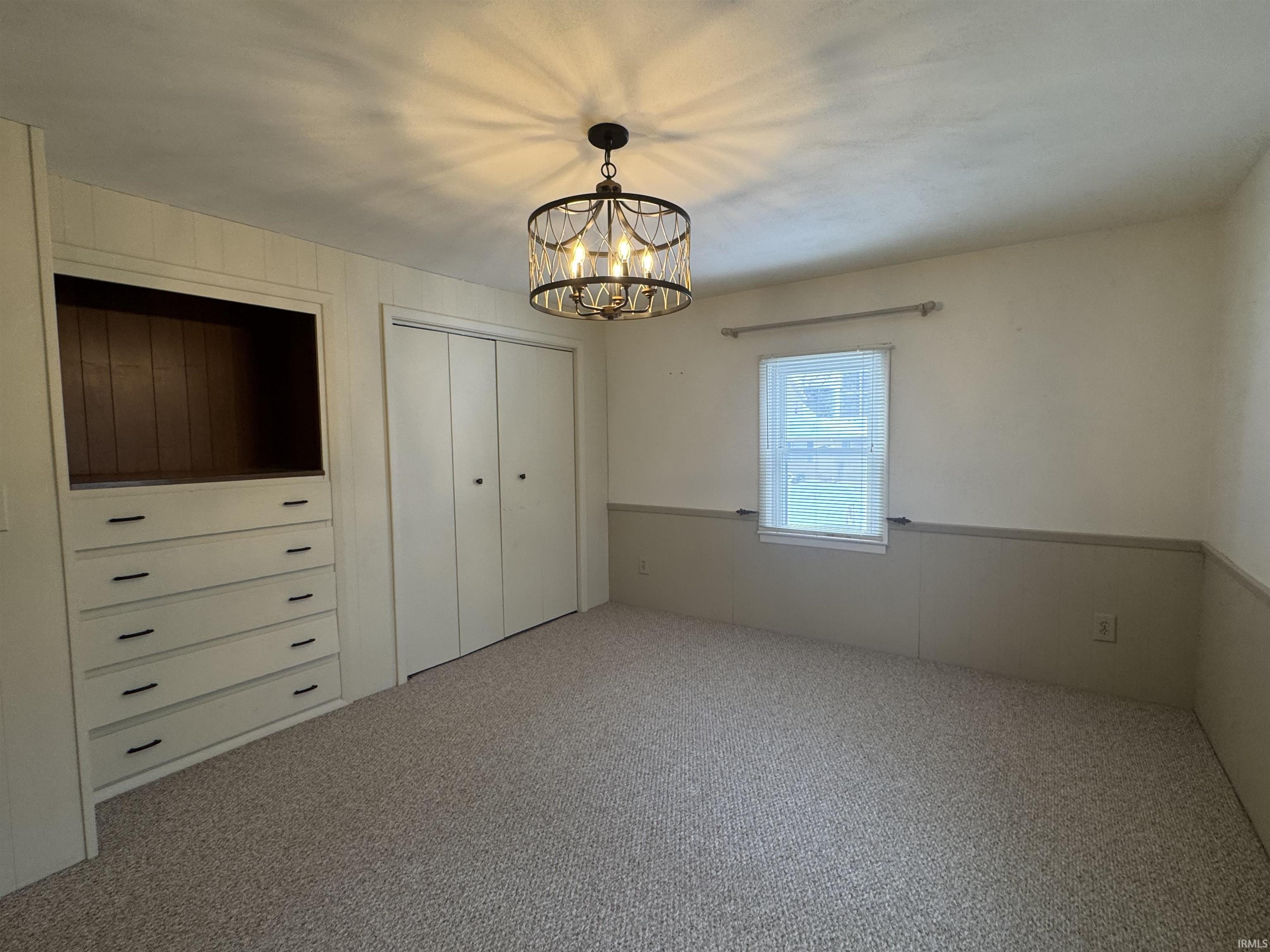 Unfurnished bedroom featuring carpet flooring, a closet, wood walls, and a chandelier
