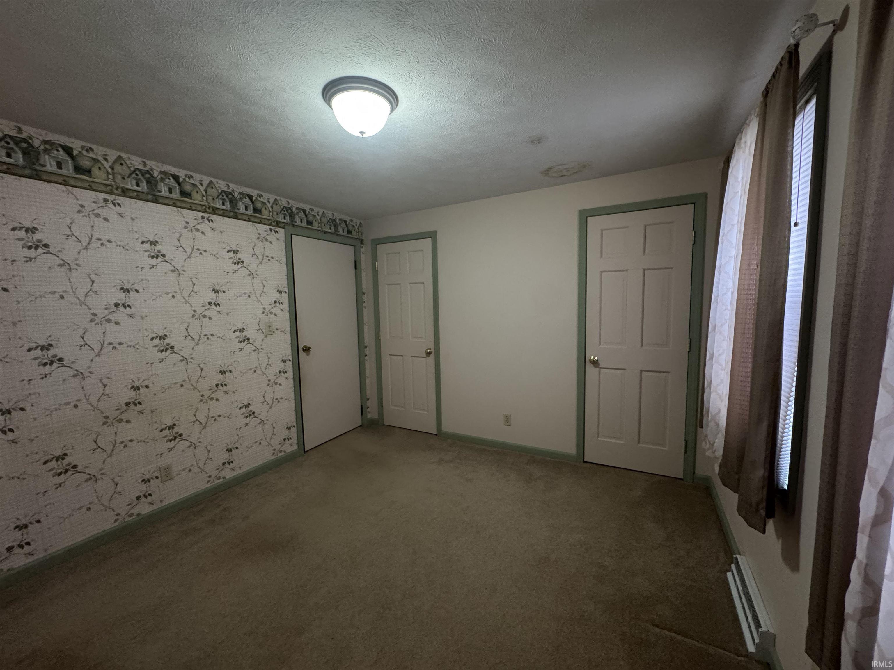 Unfurnished bedroom with wallpapered walls, carpet, a textured ceiling, and an accent wall