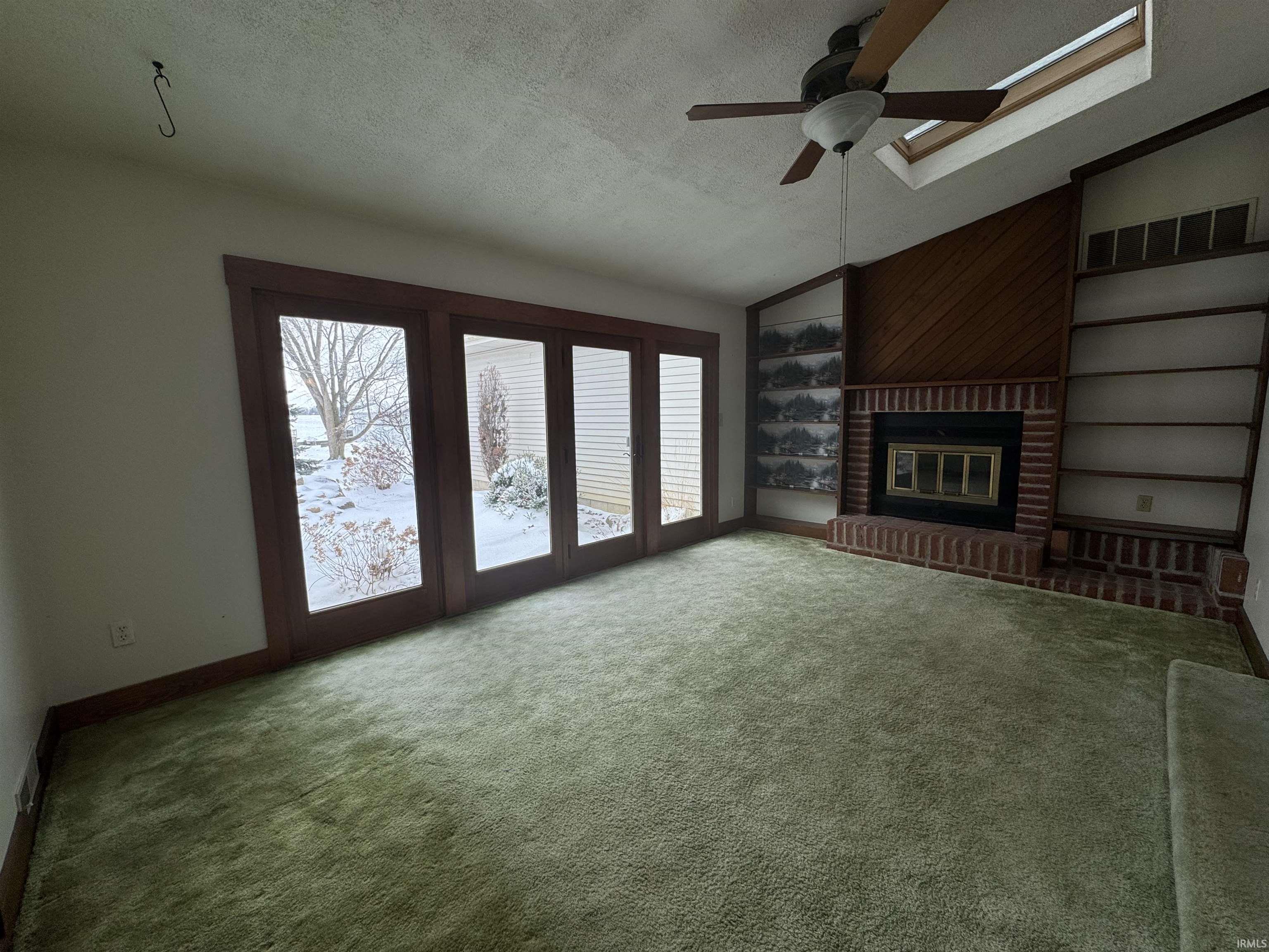 Unfurnished living room featuring built in features, a textured ceiling, ceiling fan, a brick fireplace, and carpet