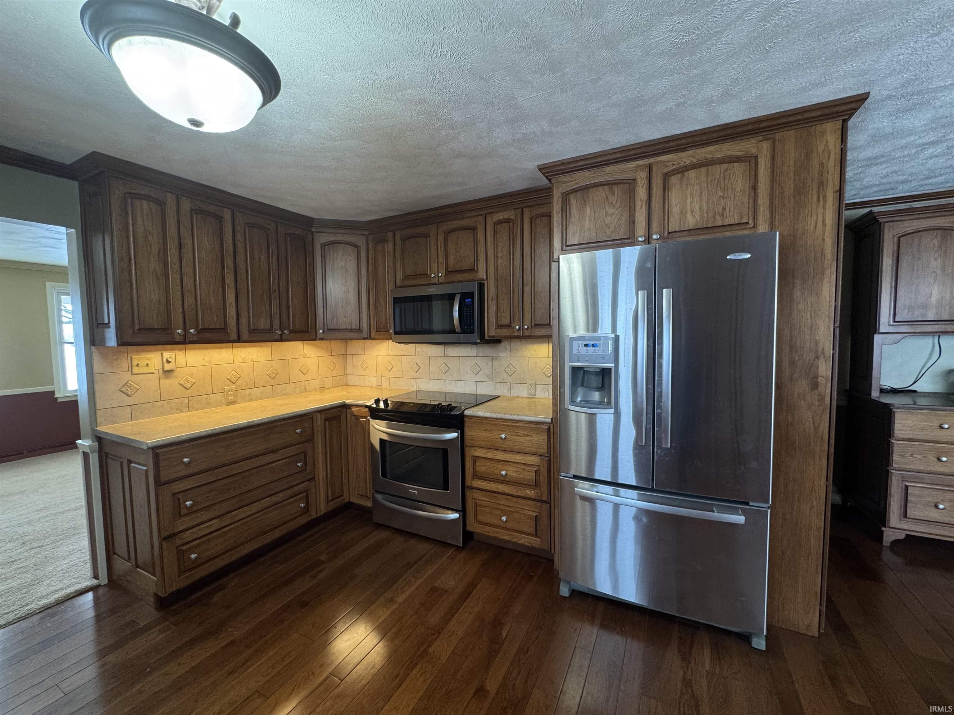 Kitchen with stainless steel appliances, dark wood-type flooring, decorative backsplash, a textured ceiling, and dark brown cabinets