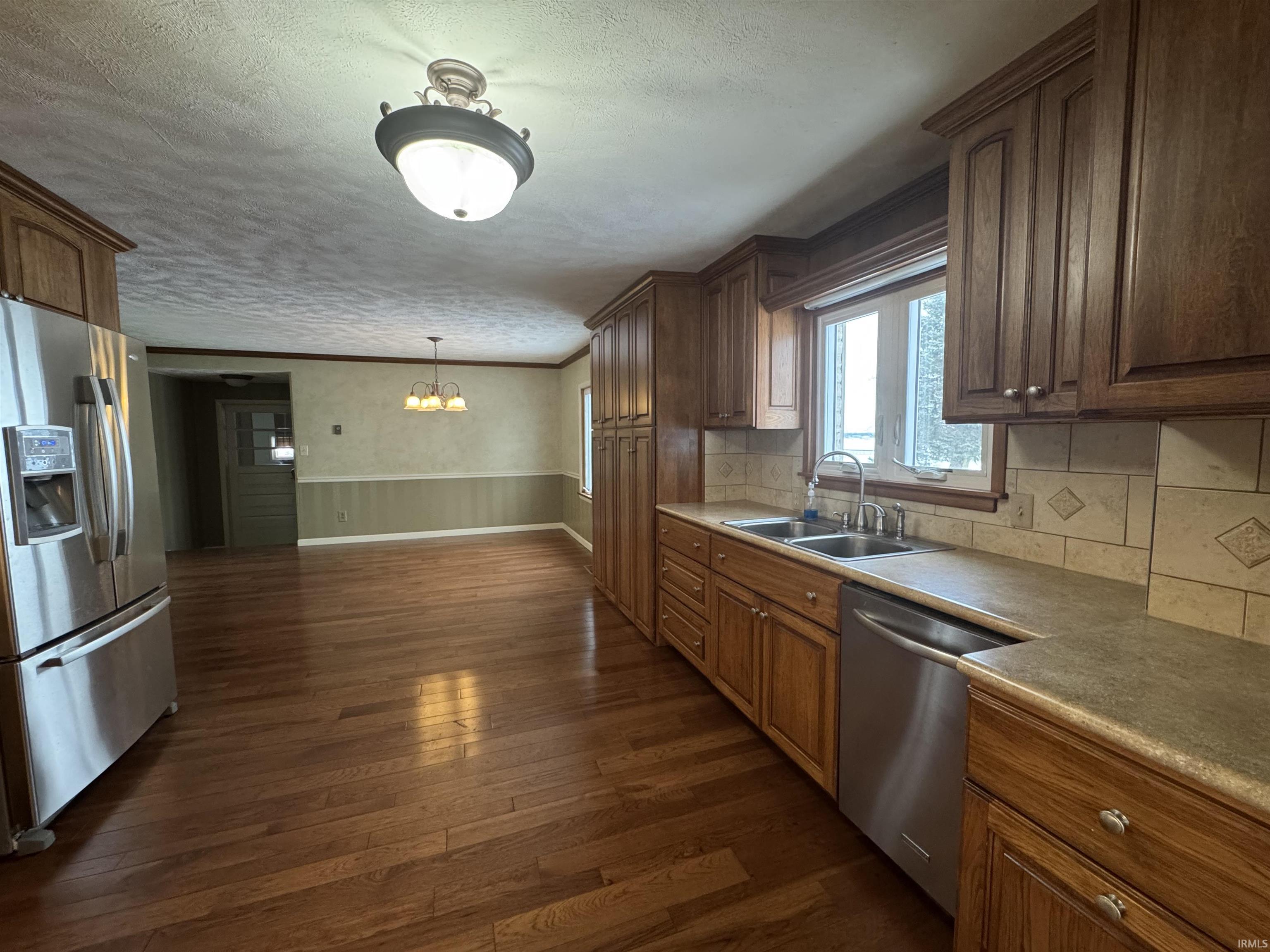 Kitchen with stainless steel appliances, dark wood-style flooring, ornamental molding, a chandelier, and a textured ceiling