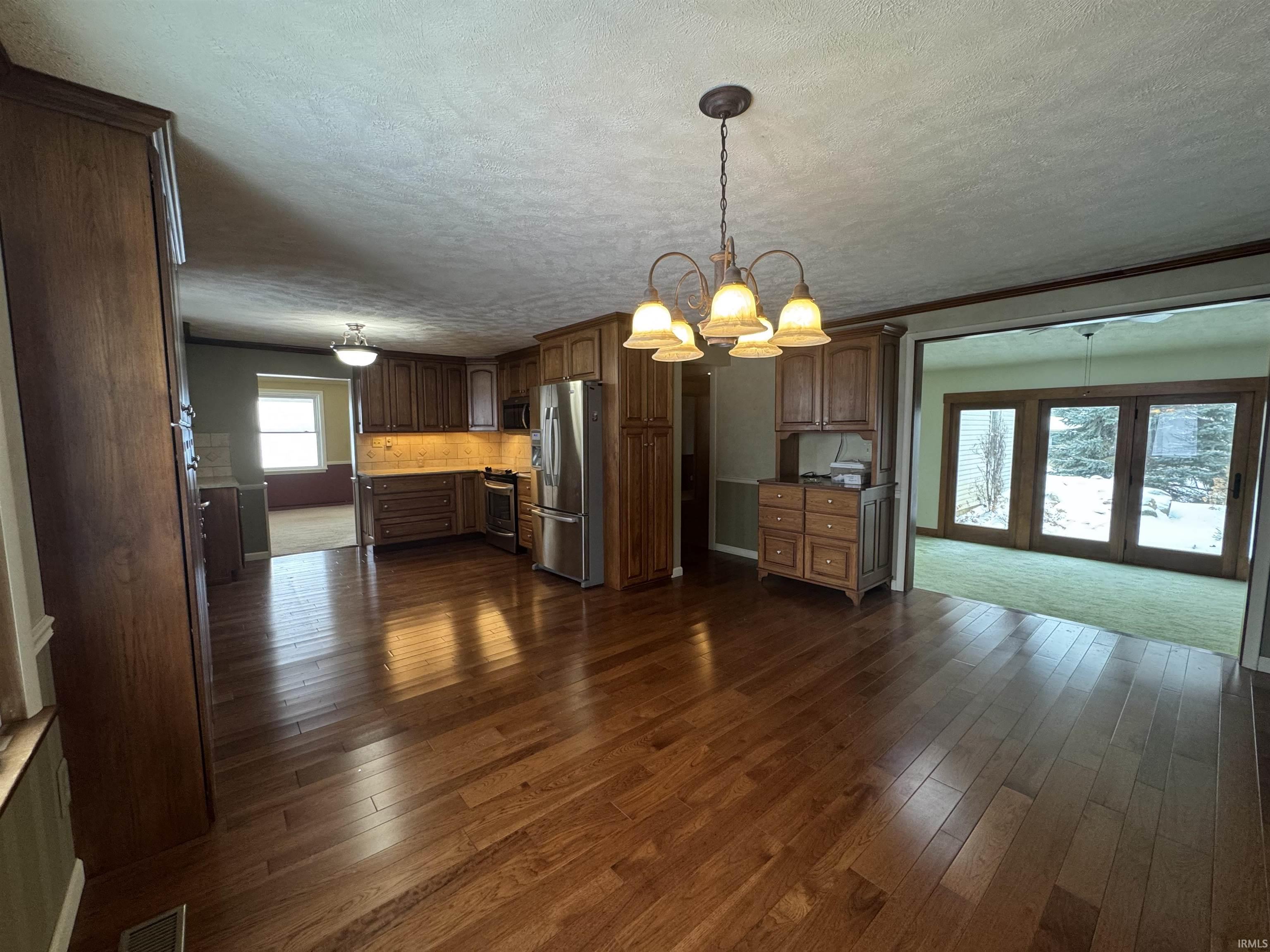 Kitchen featuring decorative light fixtures, a textured ceiling, appliances with stainless steel finishes, dark wood finished floors, and a chandelier