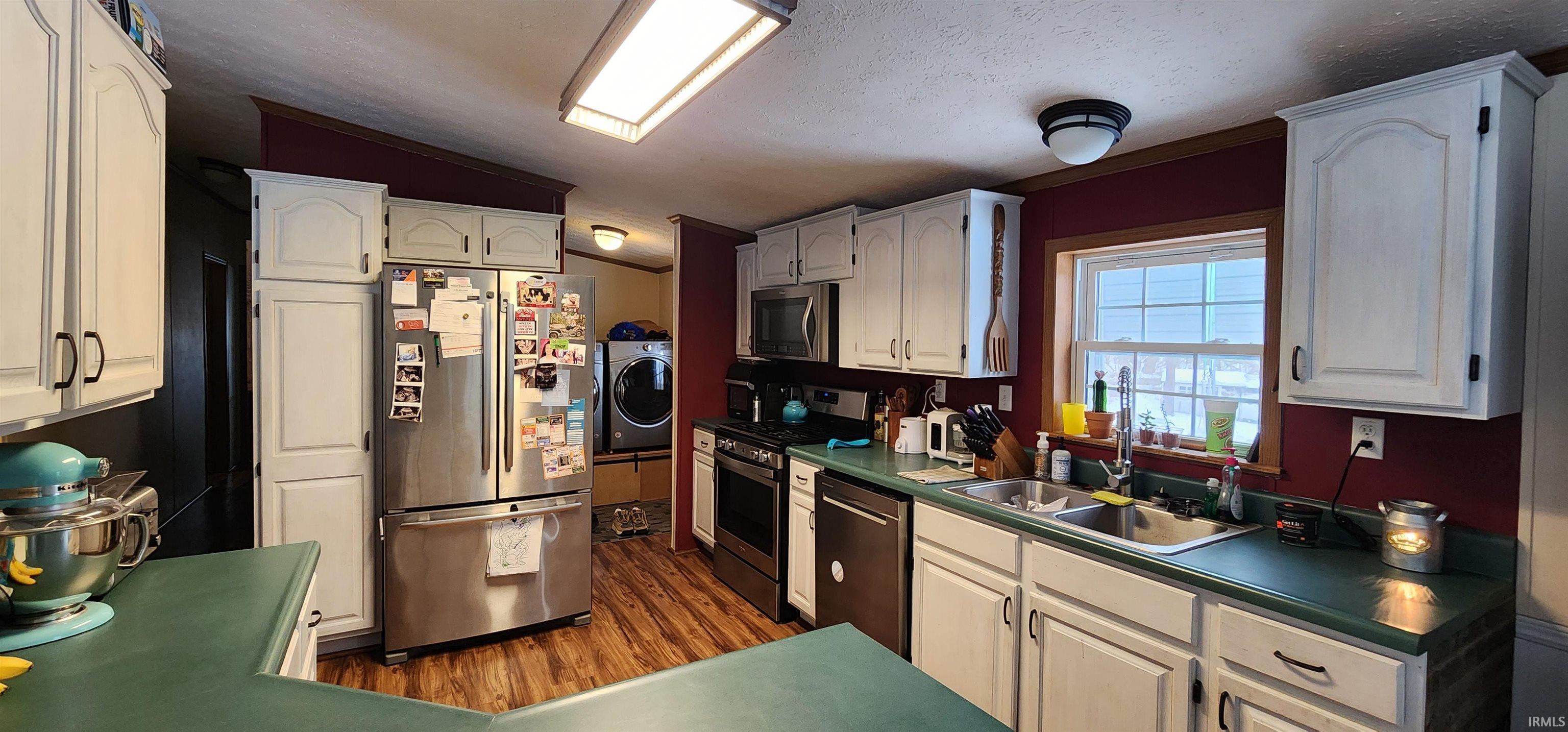 Kitchen featuring stainless steel appliances, white cabinets, dark wood-type flooring, washer / clothes dryer, and dark countertops