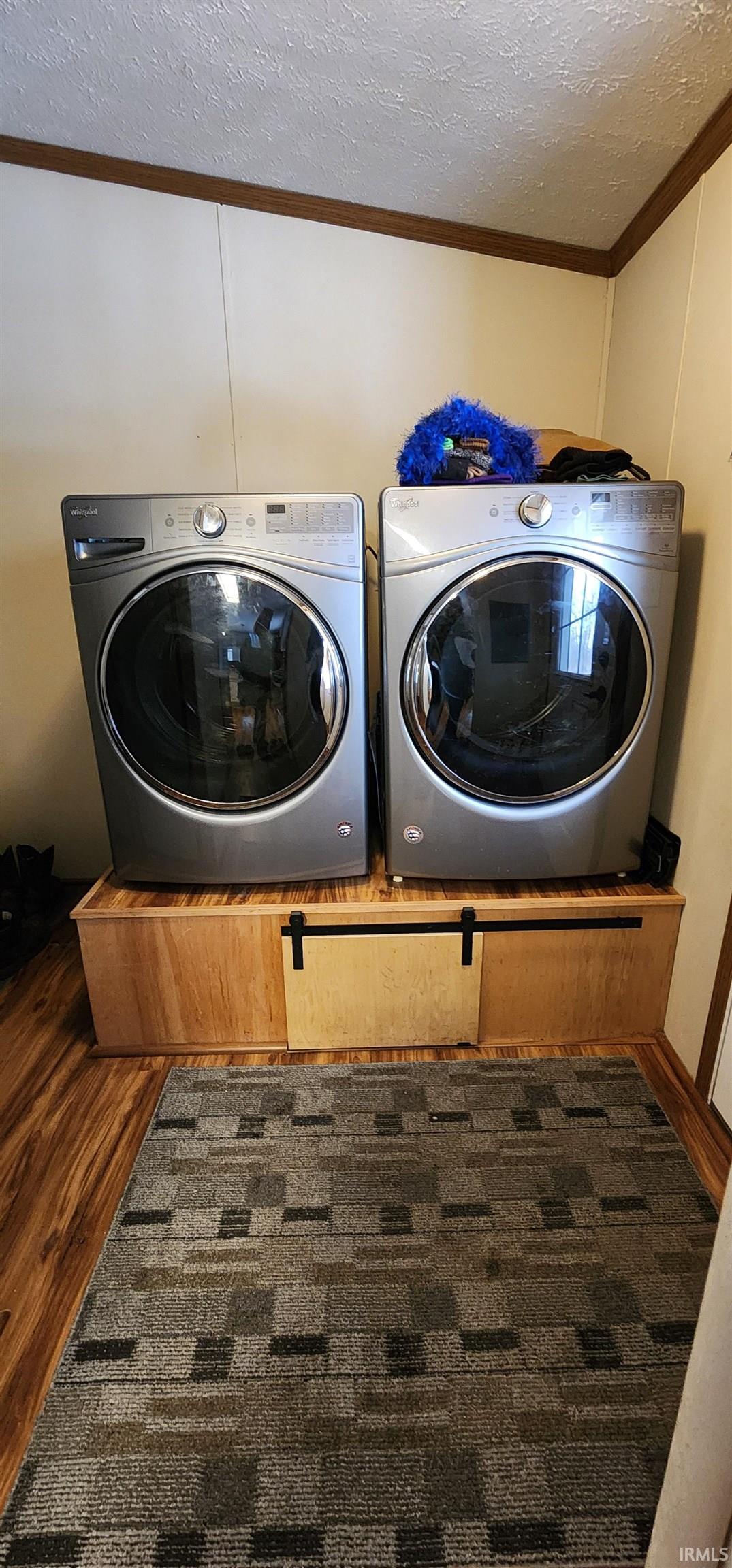 Laundry room featuring a textured ceiling, dark wood finished floors, crown molding, and washer and clothes dryer