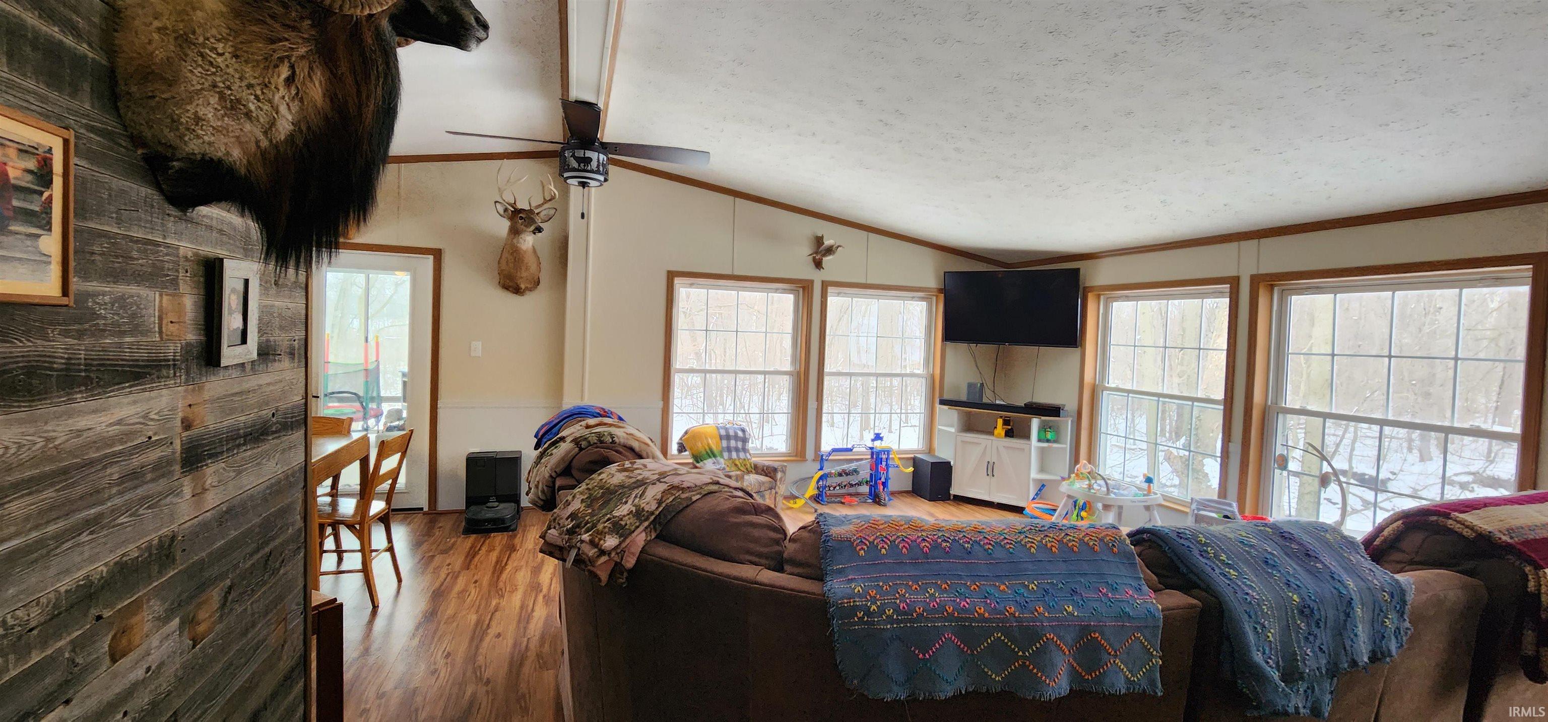 Living area featuring lofted ceiling with beams, wood finished floors, a ceiling fan, and ornamental molding