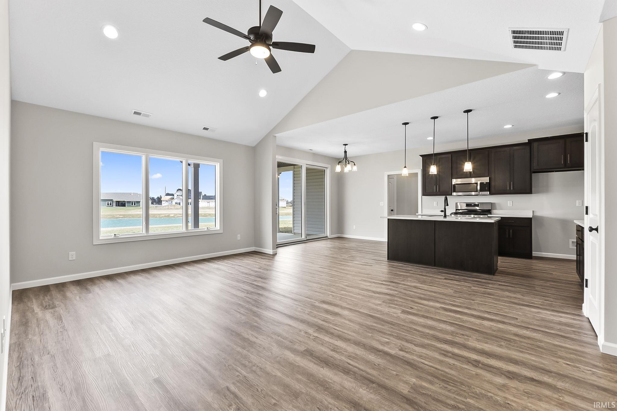 Unfurnished living room featuring ceiling fan, dark wood-type flooring, a chandelier, and a high ceiling